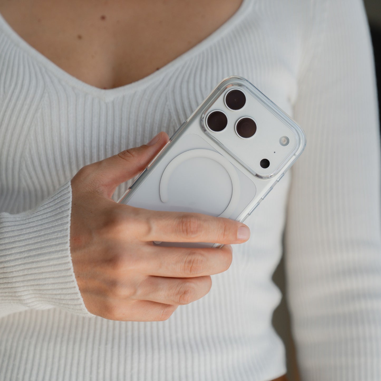 Eine Person in einem weißen Rippenoberteil hält ein iPhone 17 Pro Max mit dem arktis iPhone 17 Pro Max PureCase mit MagSafe, einer transparenten, stoßfesten Hülle von arktis, in der die Kameralinsen sichtbar sind.