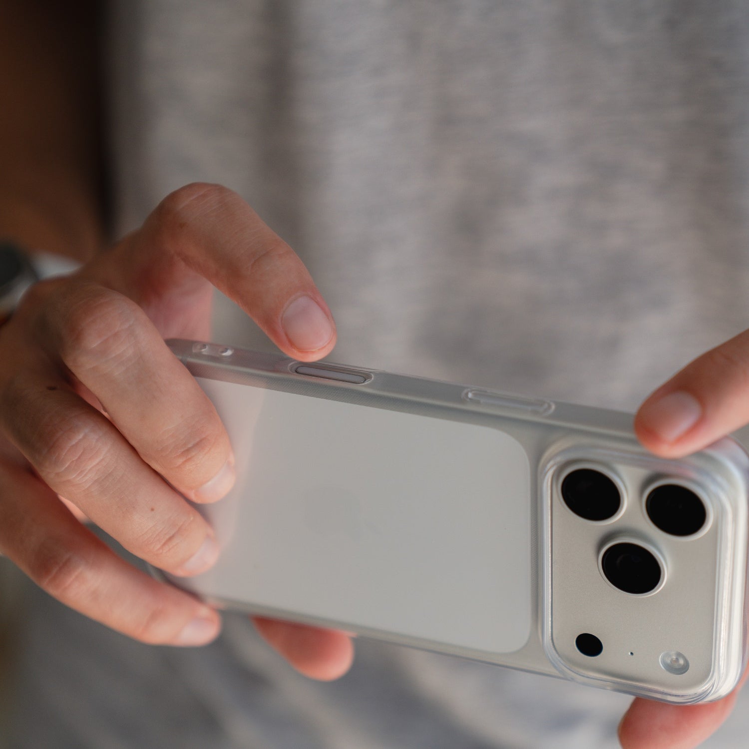 Eine Person in einem grauen Hemd hält ein Smartphone mit dem arktis iPhone 17 Pro Max ZERO Case, einer ultradünnen, transparenten Hülle von arktis.
