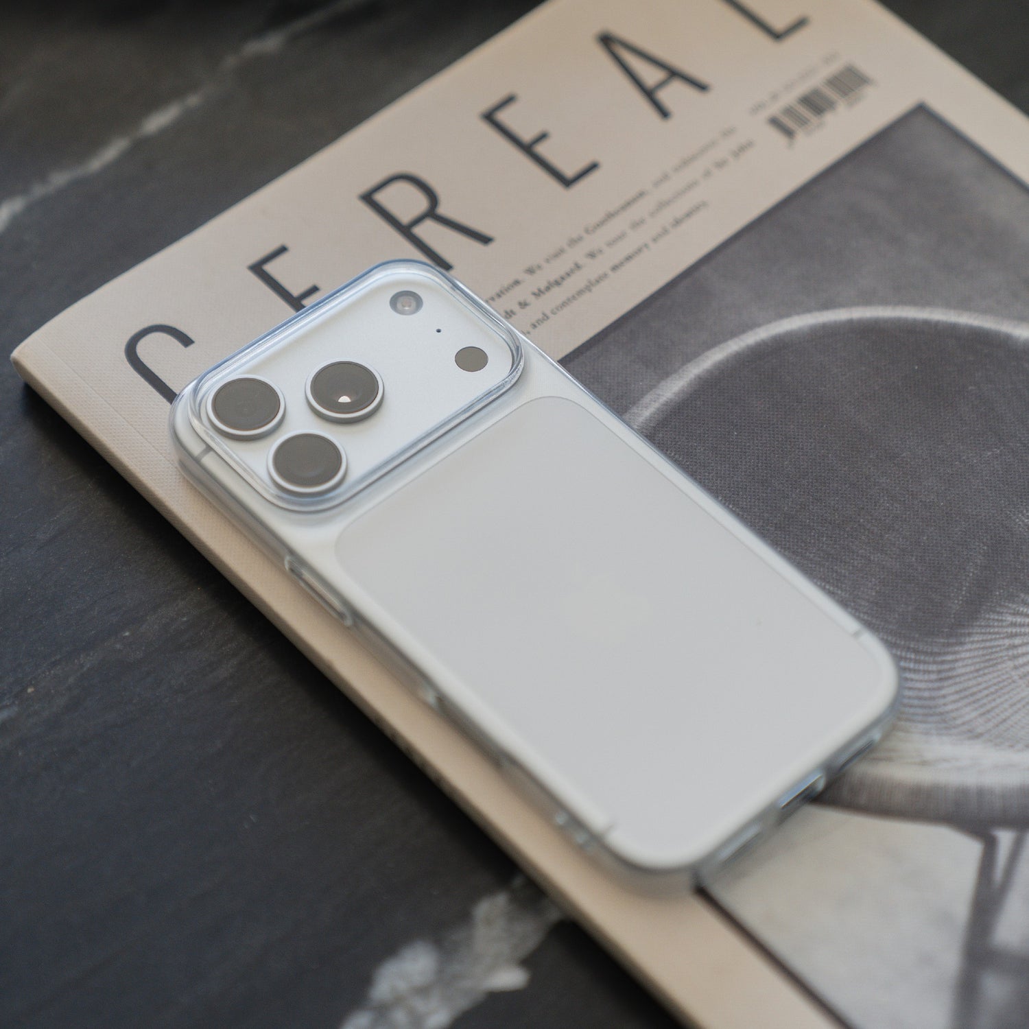 Ein iPhone 17 Pro Max mit einem arktis ZERO Case, einer schlanken, transparenten Hülle von arktis, ruht auf einem CEREAL-Magazin, das auf einer dunklen Oberfläche liegt.