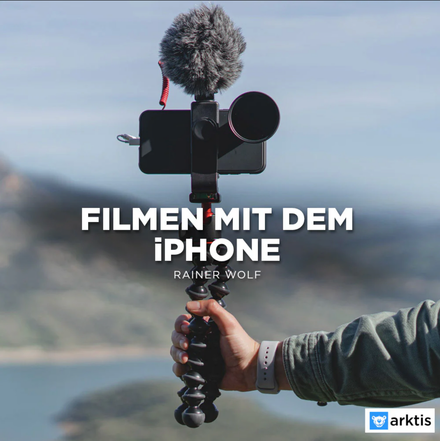 Eine Person hält ein iPhone mit externem Mikrofon auf einem Stativ. Der Text lautet „Filmen mit dem iPhone – Rainer Wolf“. Im unscharfen Landschaftshintergrund ist „professionell filmen mit der iPhone Academy von arktis.de – Grundlagen Filmen mit dem iPhone“ hervorgehoben.