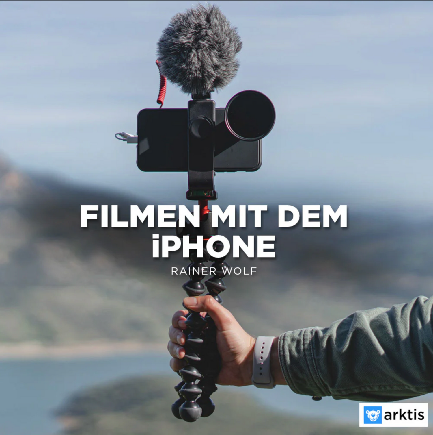 Eine Person hält ein iPhone mit externem Mikrofon auf einem Stativ. Der Text lautet „Filmen mit dem iPhone – Rainer Wolf“. Im unscharfen Landschaftshintergrund ist „professionell filmen mit der iPhone Academy von arktis.de – Grundlagen Filmen mit dem iPhone“ hervorgehoben.