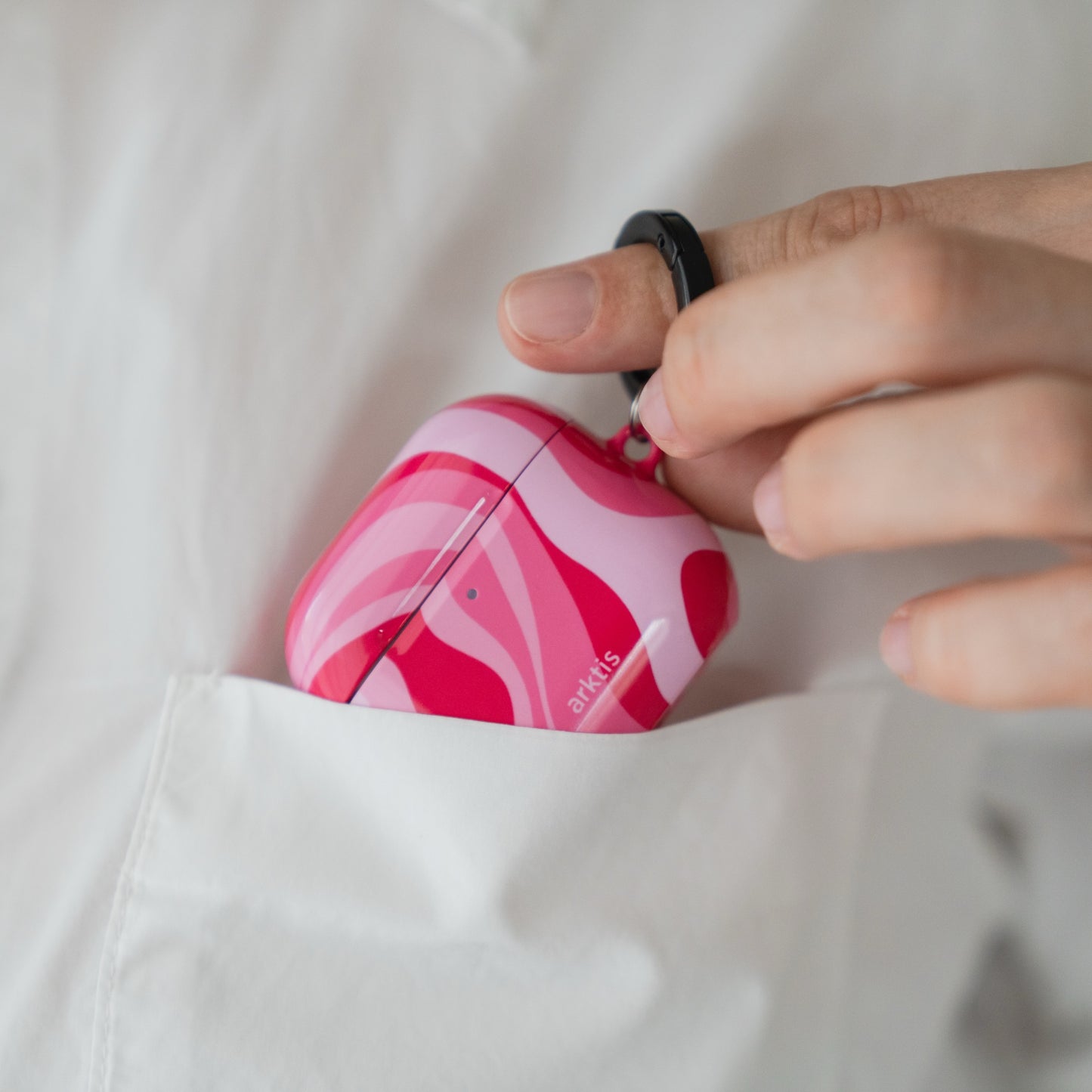 Arktis AirPods Pro 3-Hülle – Aura Pink mit einem schwarzen Schlüsselanhänger, gesteckt in die Tasche eines weißen Hemdes.