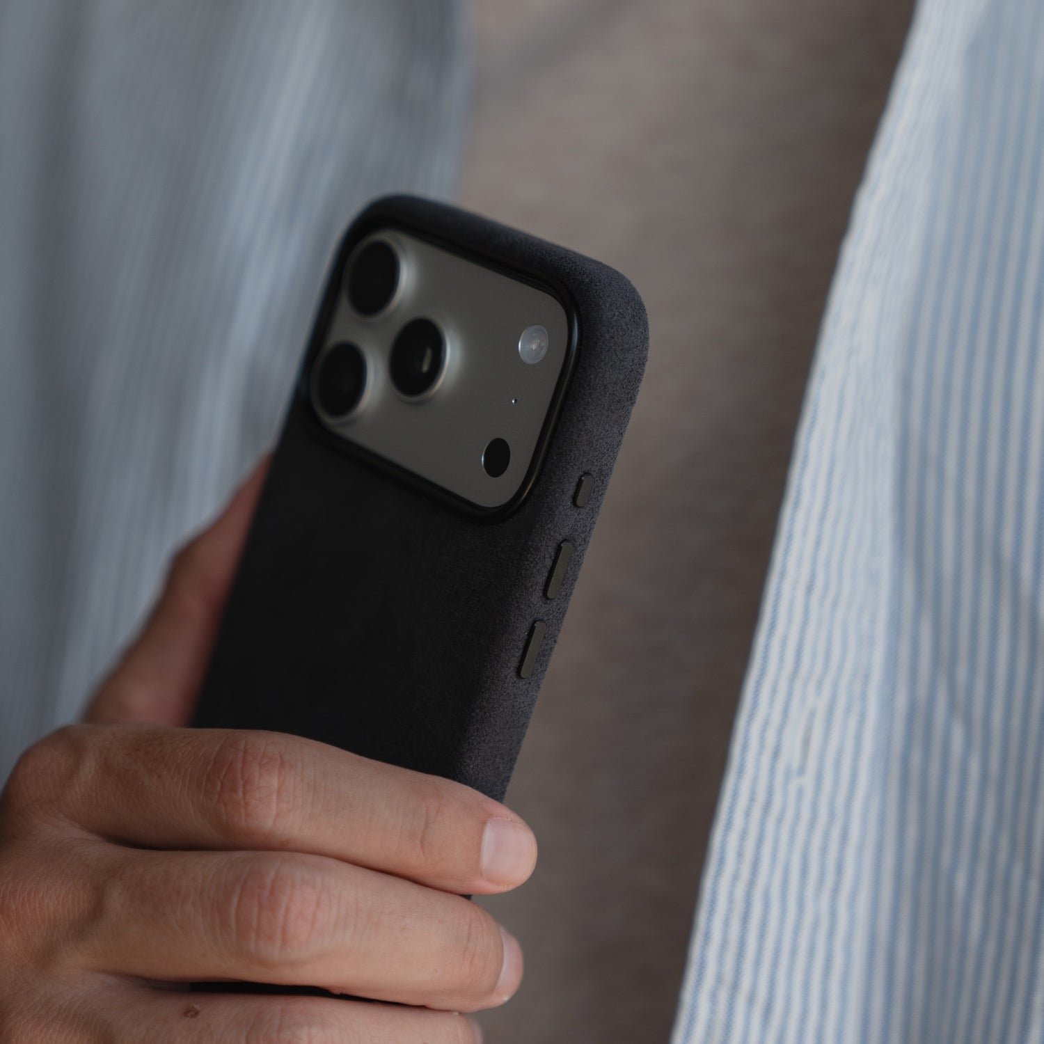 Eine Person hält ein Smartphone mit einer arktis iPhone 17 Pro Hülle aus Alcantara von arktis und trägt ein hellblau-weiß gestreiftes Hemd.