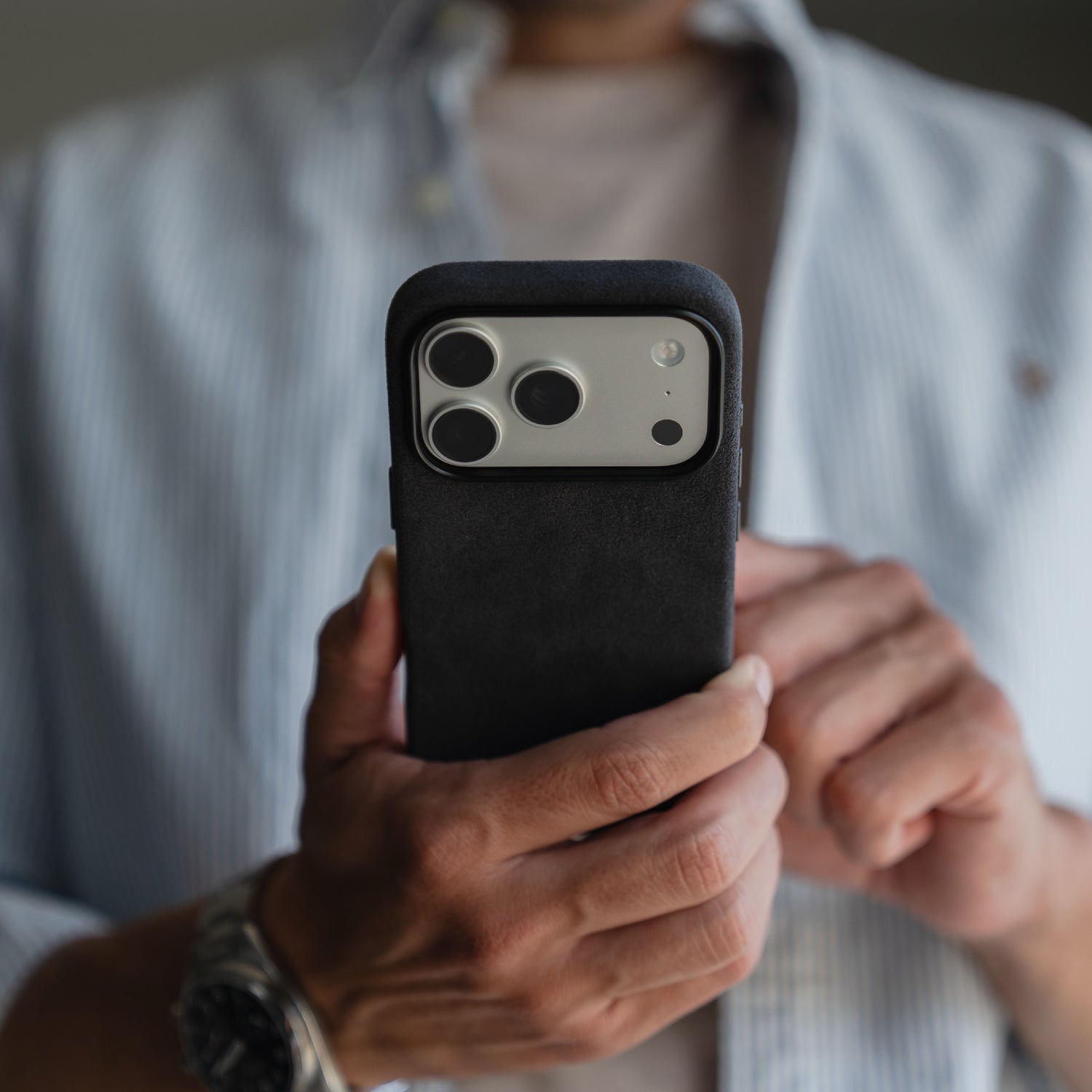 Eine Person in einem blauen Hemd hält ein Smartphone mit einer arktis iPhone 17 Pro Hülle aus Alcantara von arktis, die Kameralinsen zeigen nach vorne.