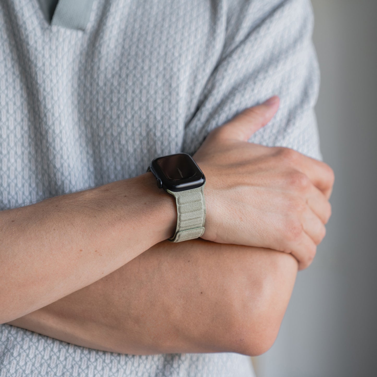 Er trägt das arktisband Apple Watch magnetisches Armband aus Alcantara in Hellgrau, die Arme über einem gemusterten Hemd verschränkt - eine subtile Anspielung auf italienisches Lifestyle-Flair.
