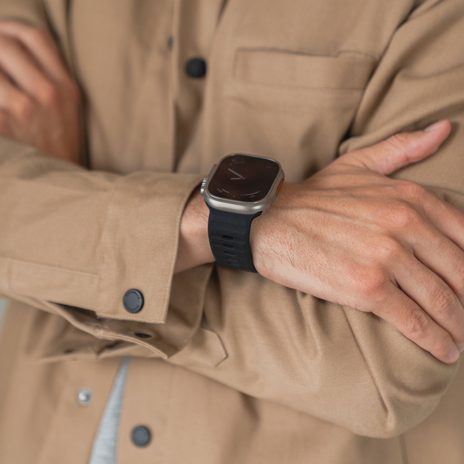 Eine Person in einem hellbraunen Hemd mit Knopfleiste verschränkt die Arme und zeigt ein Arktisband Apple Watch Silikonarmband „Active“ für verbesserte Atmungsaktivität.