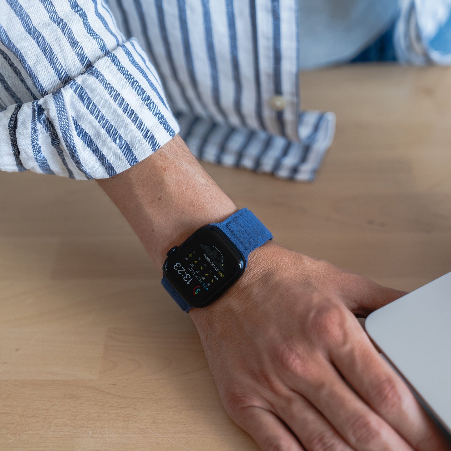 Jemand trägt ein arktisband Apple Watch magnetisches Armband aus Alcantara in blau, legt die Hand auf den Schreibtisch neben den Laptop und bringt italienisches Lebensgefühl in den Arbeitstag.