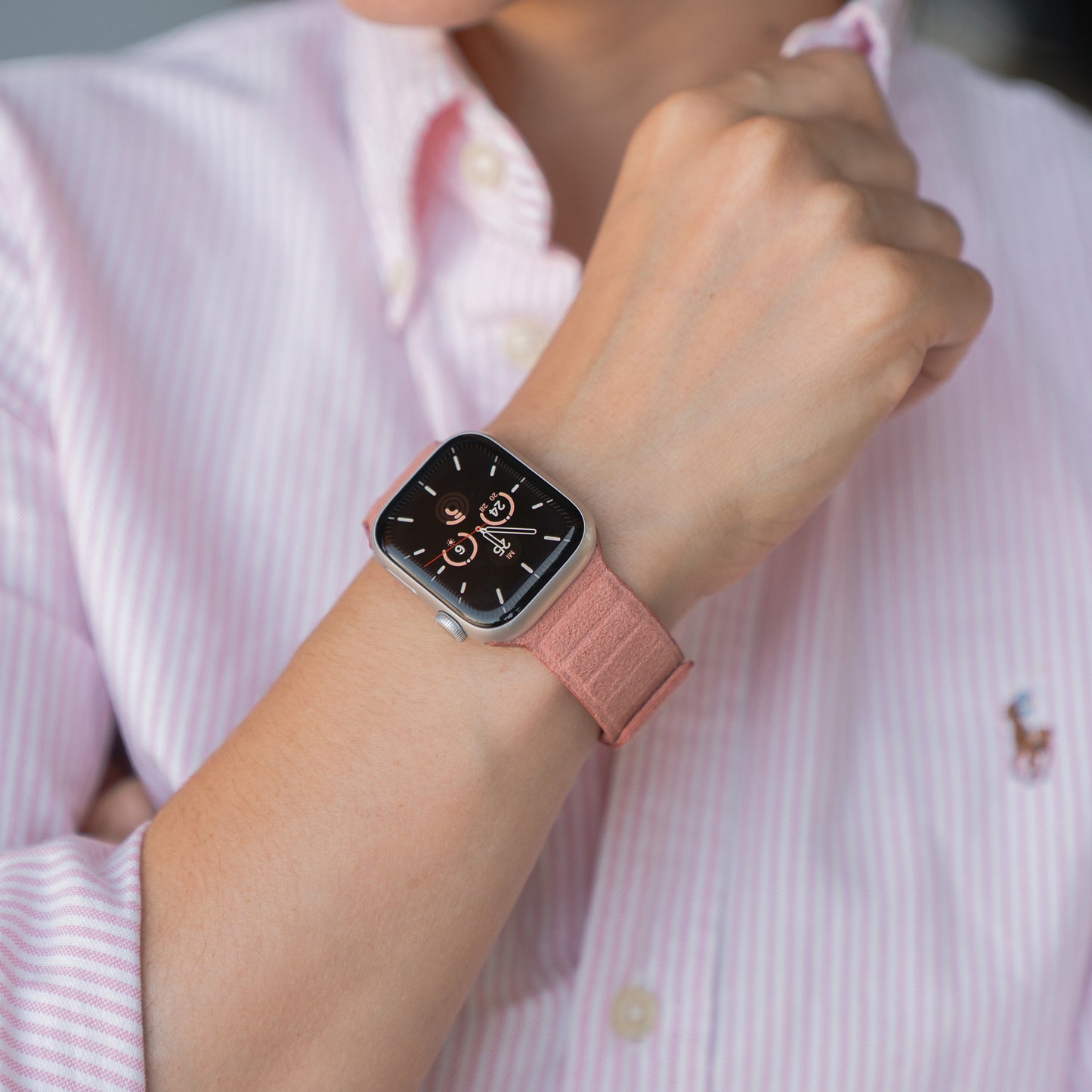 Eine Person trägt ein rosa gestreiftes Hemd und ein arktisband Apple Watch magnetisches Armband aus Alcantara von arktisband, Apple Watch kompatibel, mit einem rosa Band am Handgelenk.