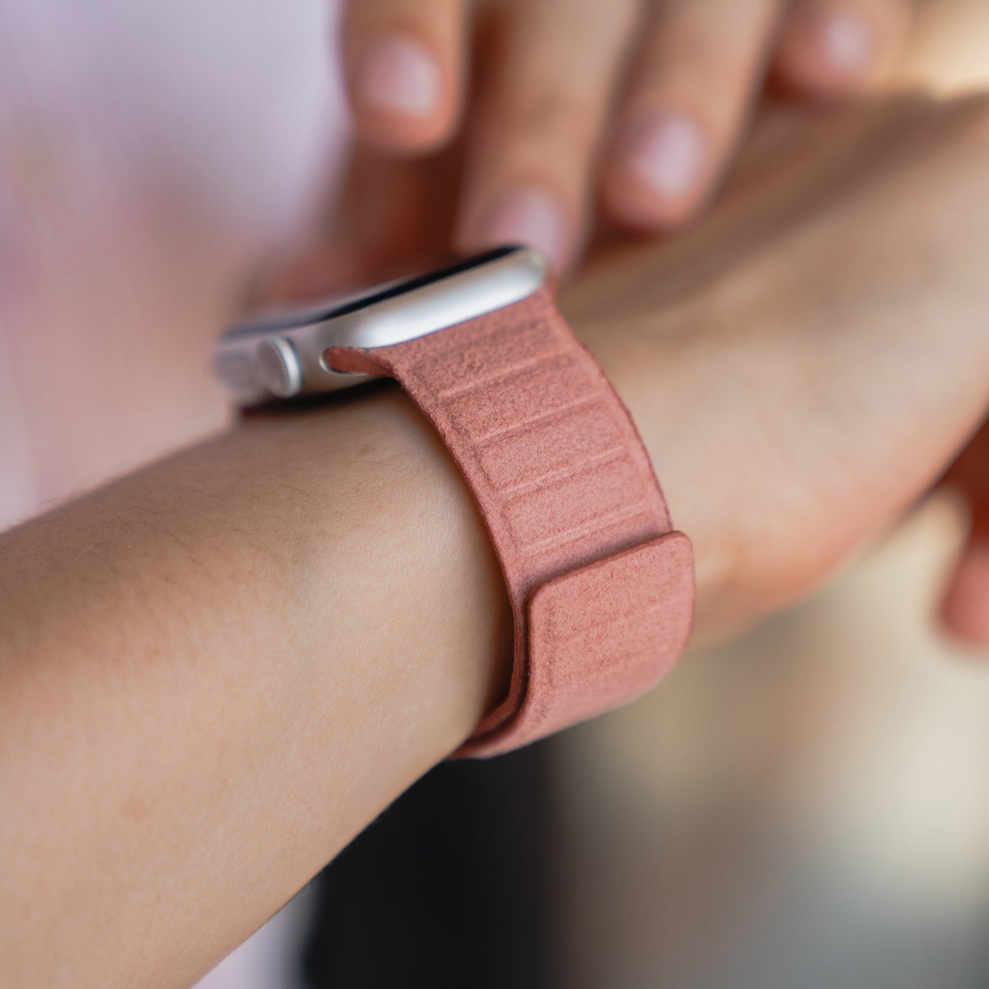 Nahaufnahme: Eine Person trägt das arktisband Apple Watch magnetisches Armband aus Alcantara mit pinkem Stoff am Handgelenk - kompatibel mit der Apple Watch, inspiriert vom italienischen Design.