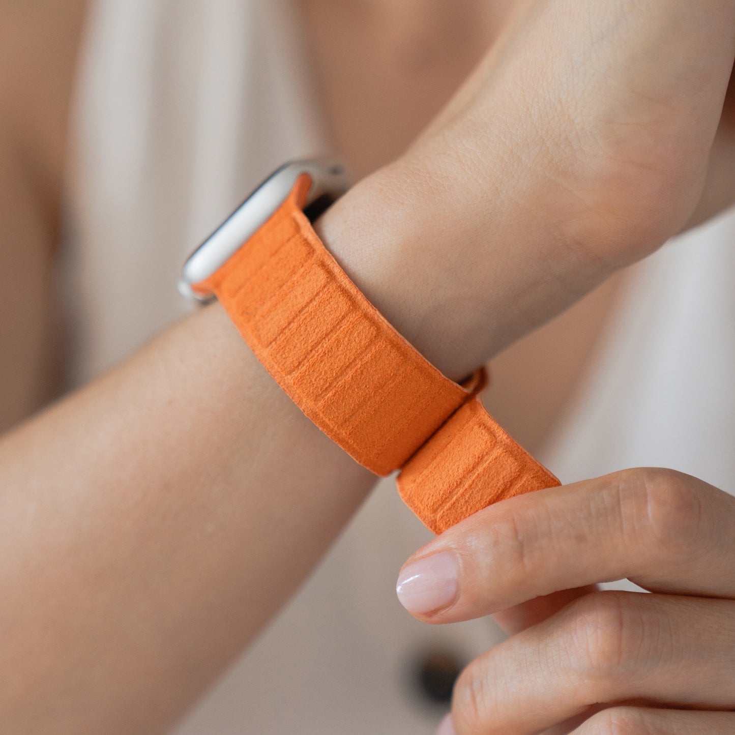 Nahaufnahme einer Person, die ein orangefarbenes Arktisband Apple Watch magnetisches Armband aus Alcantara am Handgelenk befestigt - echter italienischer Stil, kompatibel mit Apple Watch.