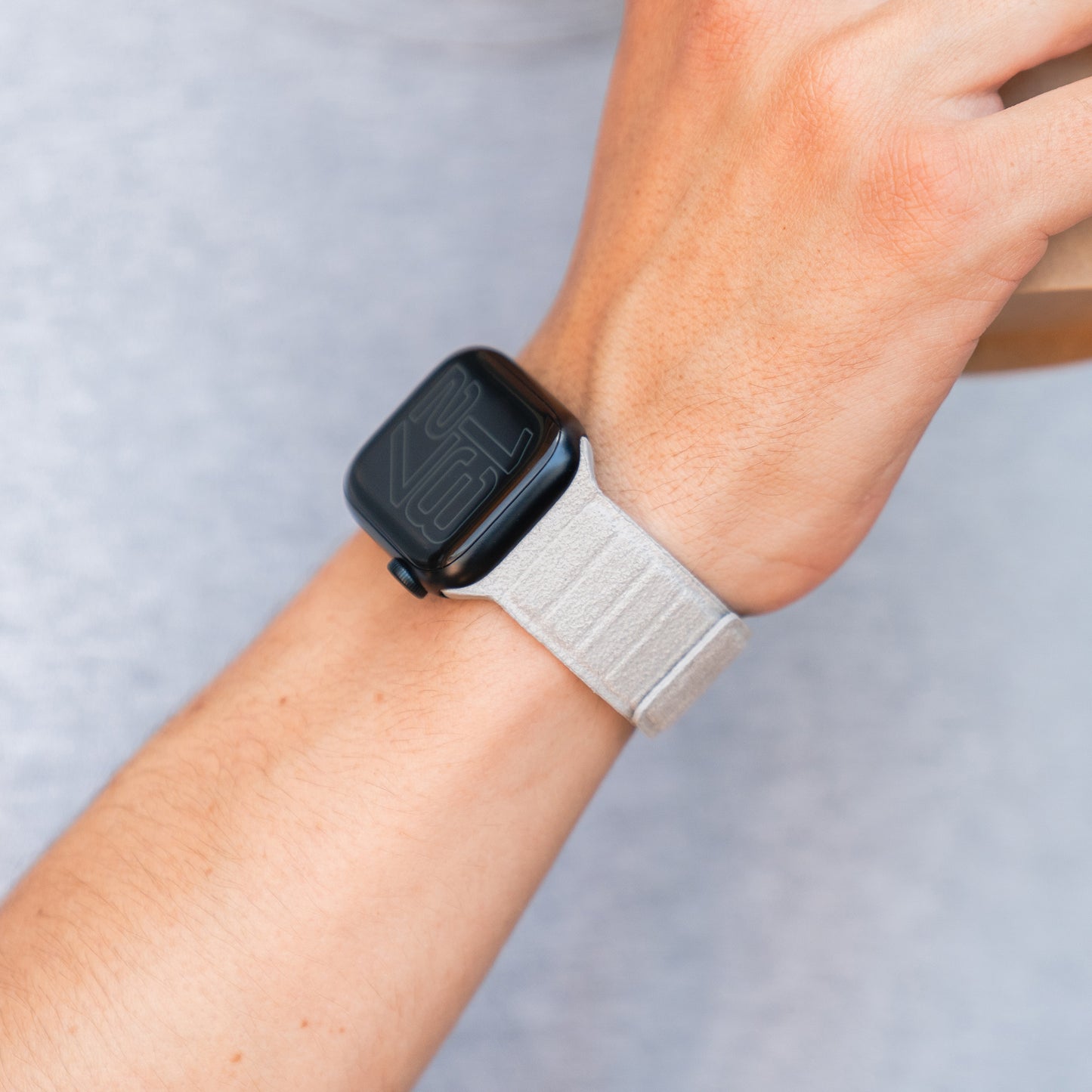 Eine Person trägt ein magnetisches Apple Watch Armband aus Alcantara in Hellgrau, das italienisches Design präsentiert.