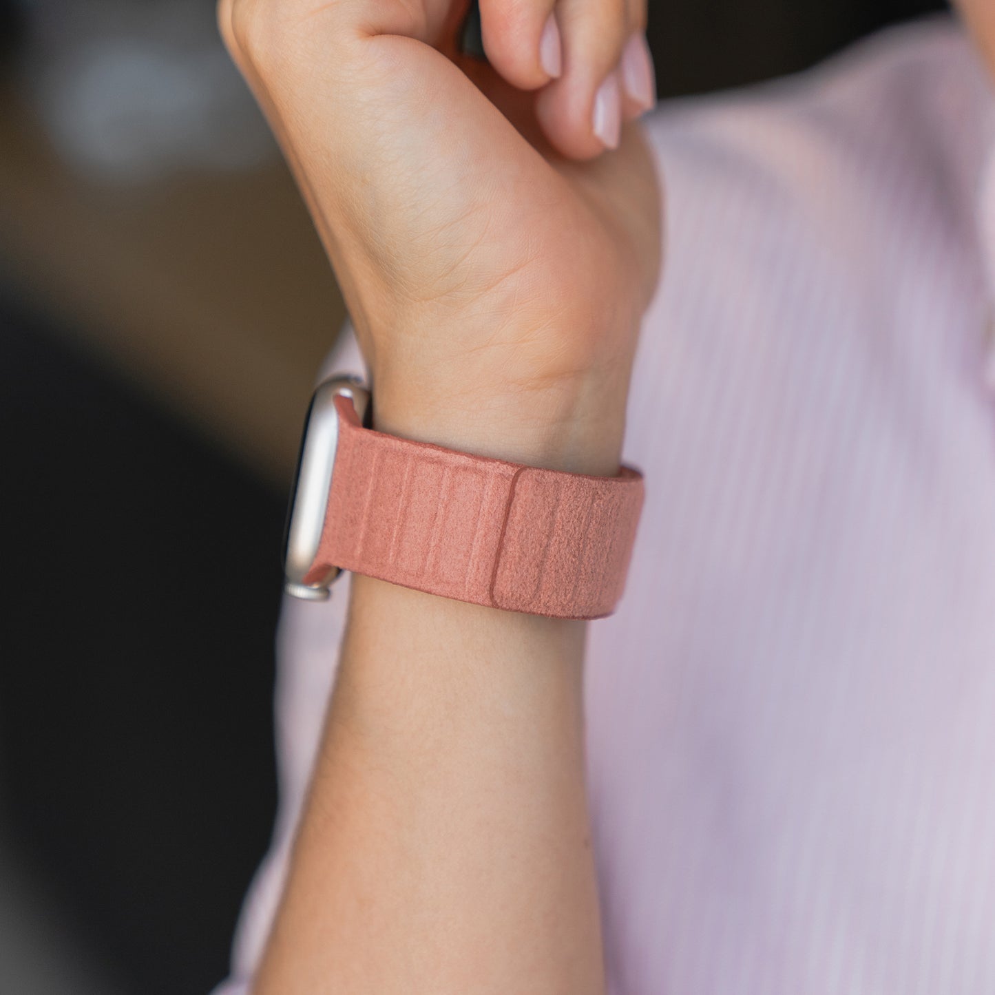 Eine Person trägt das arktisband Apple Watch magnetisches Armband aus Alcantara in Pink an ihrem Handgelenk, gestylt mit einem hellrosa Hemd - ein elegantes Accessoire von arktisband mit italienischem Design und Apple Watch Kompatibilität.