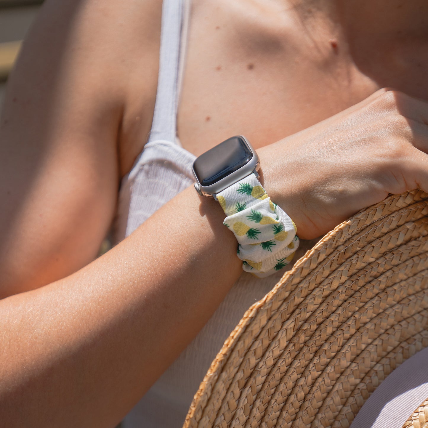 Jemand, der das arktisband Apple Watch Scrunchie Armband "Elanora" trägt, hält einen Strohhut im Sonnenlicht.