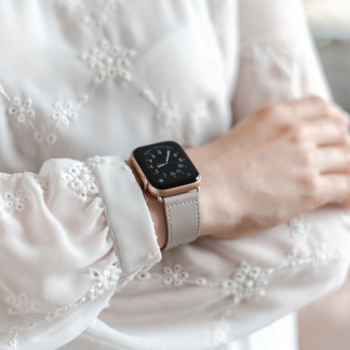 Eine Person trägt eine langärmelige, bestickte weiße Bluse und ein Arktisband Apple Watch Lederarmband „Novus“ am Handgelenk, wodurch minimalistischer Look mit maximalem Tragekomfort verbunden wird, da sie die Arme verschränkt.