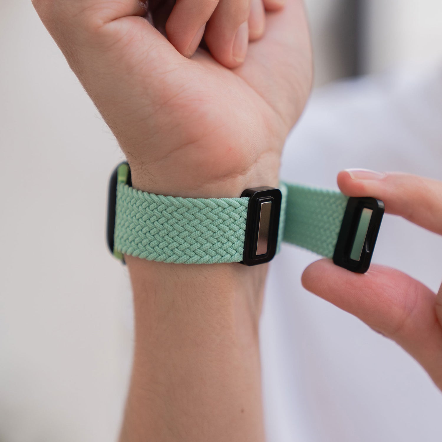 Eine Person befestigt ein arktisband Geflochtenes Apple Watch Armband „Casual“ in Hellgrün mit schwarzem Magnetverschluss um ihr Handgelenk.