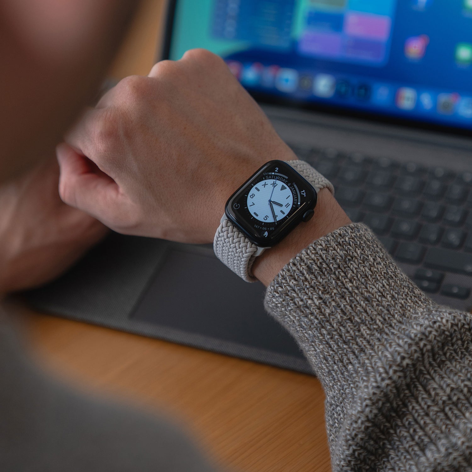 Eine Person überprüft ihr arktisband Geflochtenes Apple Watch Armband "Casual" mit Magnetverschluss von arktisband, während sie an ihrem Schreibtisch an einem Laptop arbeitet.