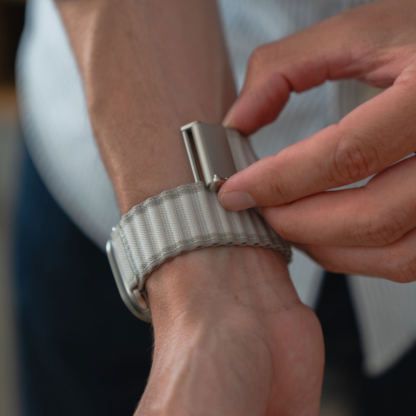 Eine Person befestigt das arktisband Apple Watch Nylon Armband „Venture“ mit der rechten Hand am Handgelenk und trägt dabei ein helles Langarmshirt – perfekt für Outdoor-Fans.