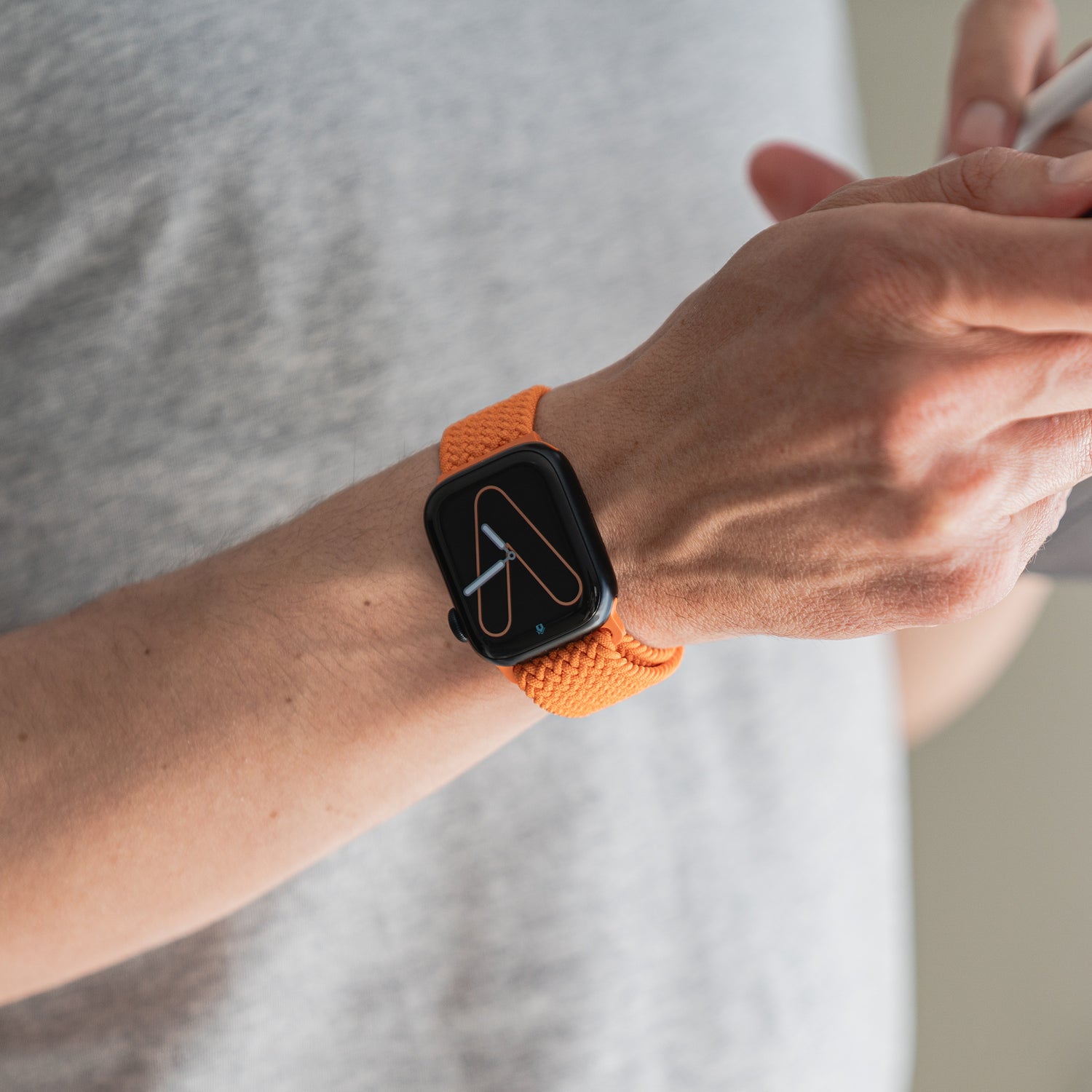 Eine Person trägt ein von arktisband geflochtenes Apple Watch Armband „Casual“ mit Magnetverschluss in Orange von arktisband und nutzt ein Smartphone.