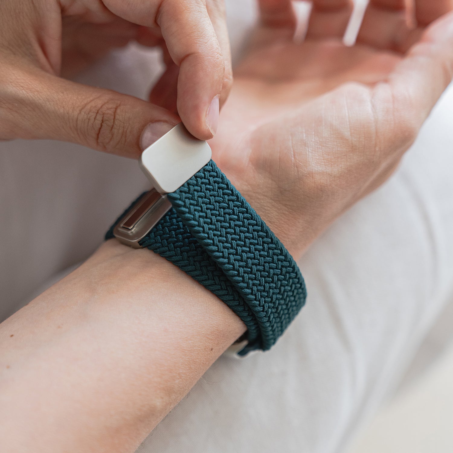 Eine Person befestigt das blaue arktisband Geflochtene Apple Watch Armband „Casual“ mit einem weißen Magnetverschluss von arktisband am Handgelenk.