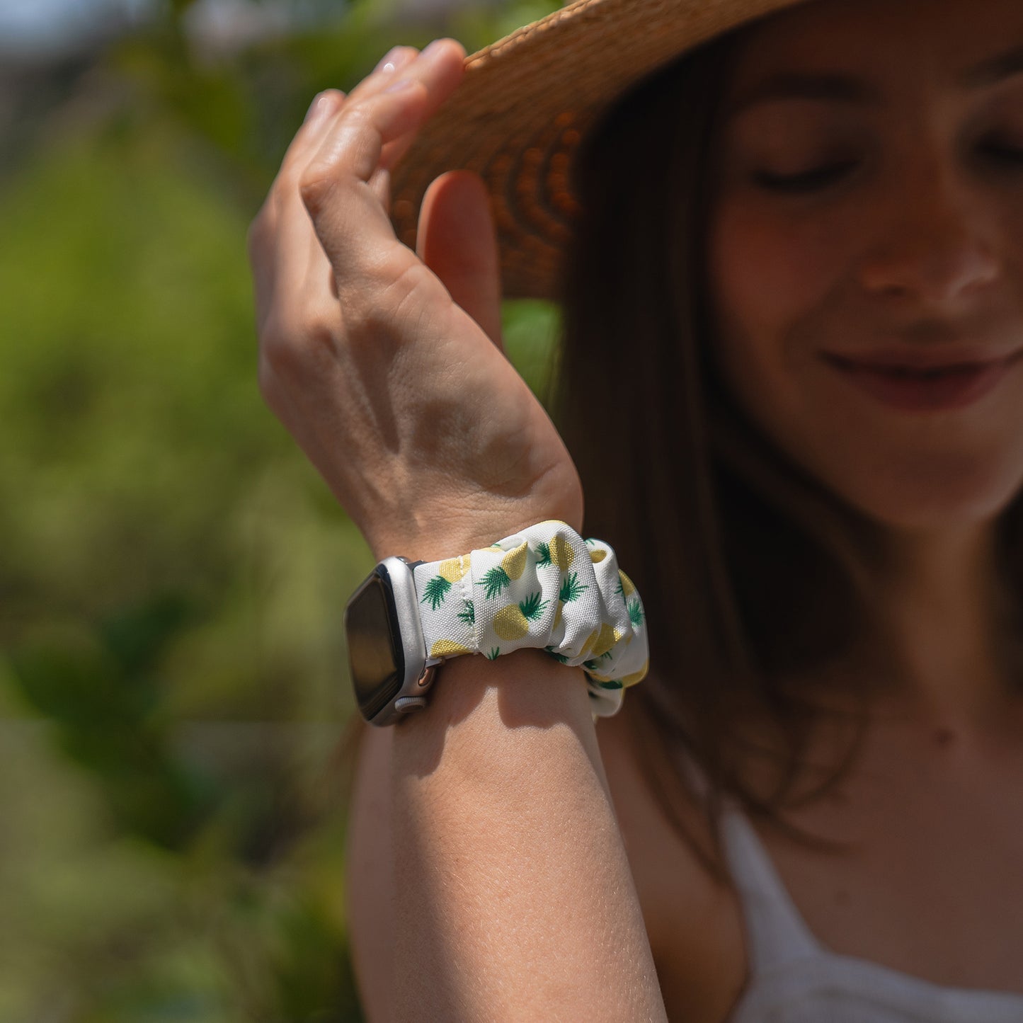Eine Frau mit Sonnenhut zeigt ihr Arktisband Apple Watch Scrunchie Armband "Elanora" mit Ananas-Muster im Freien.