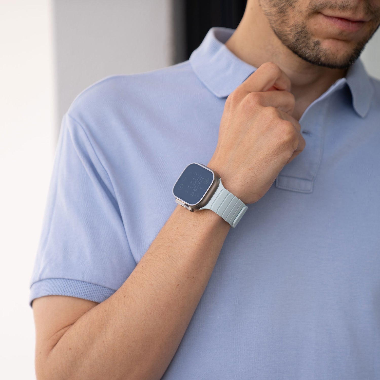 Mann im hellblauen Poloshirt trägt das Arktisband Apple Watch Magnetarmband „MagFlow“ mit hellblauem Silikonband am linken Handgelenk.
