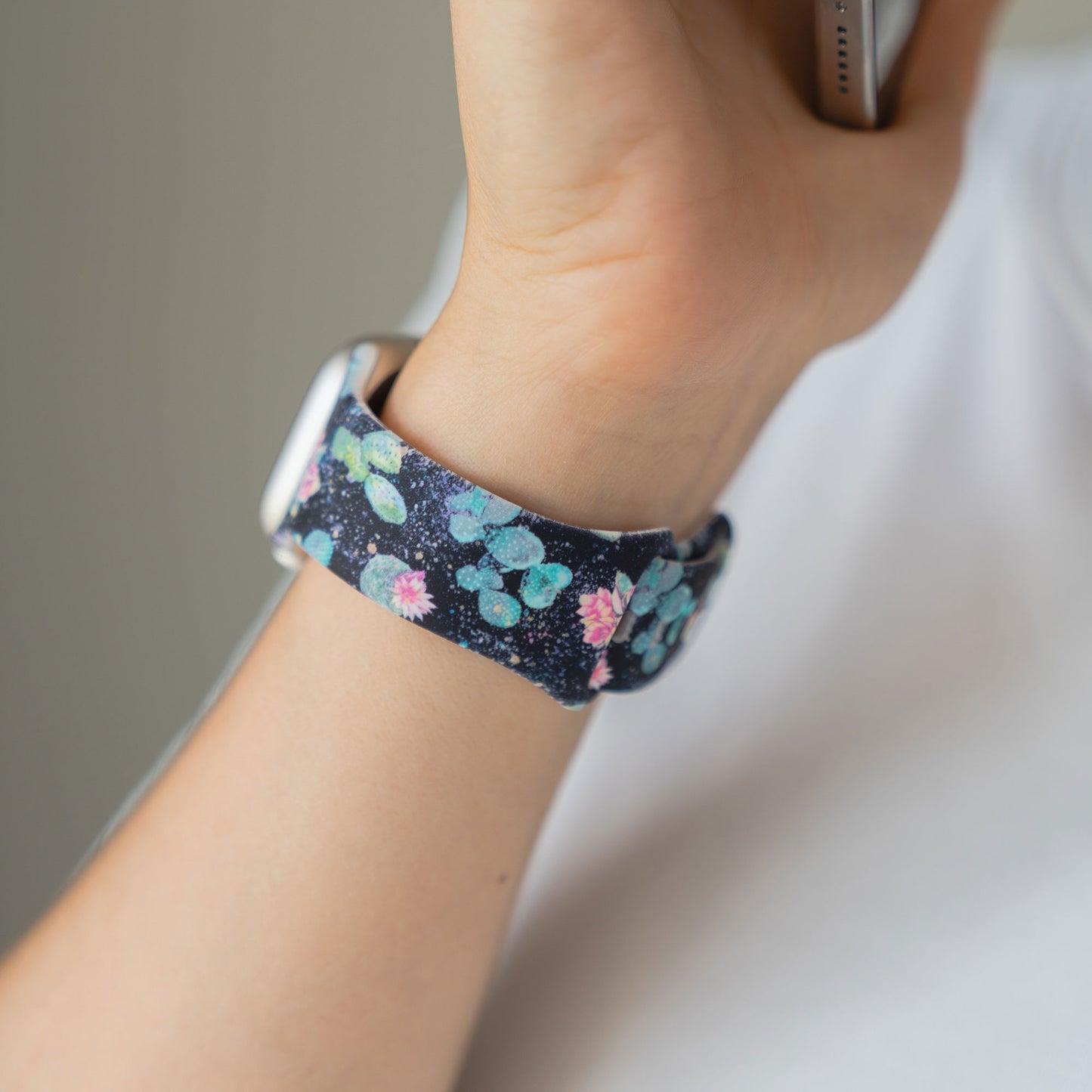 Eine Person trägt eine arktisband EDITION für Apple Watch mit einem blauen, blumengemusterten Band und hält ein Telefon.