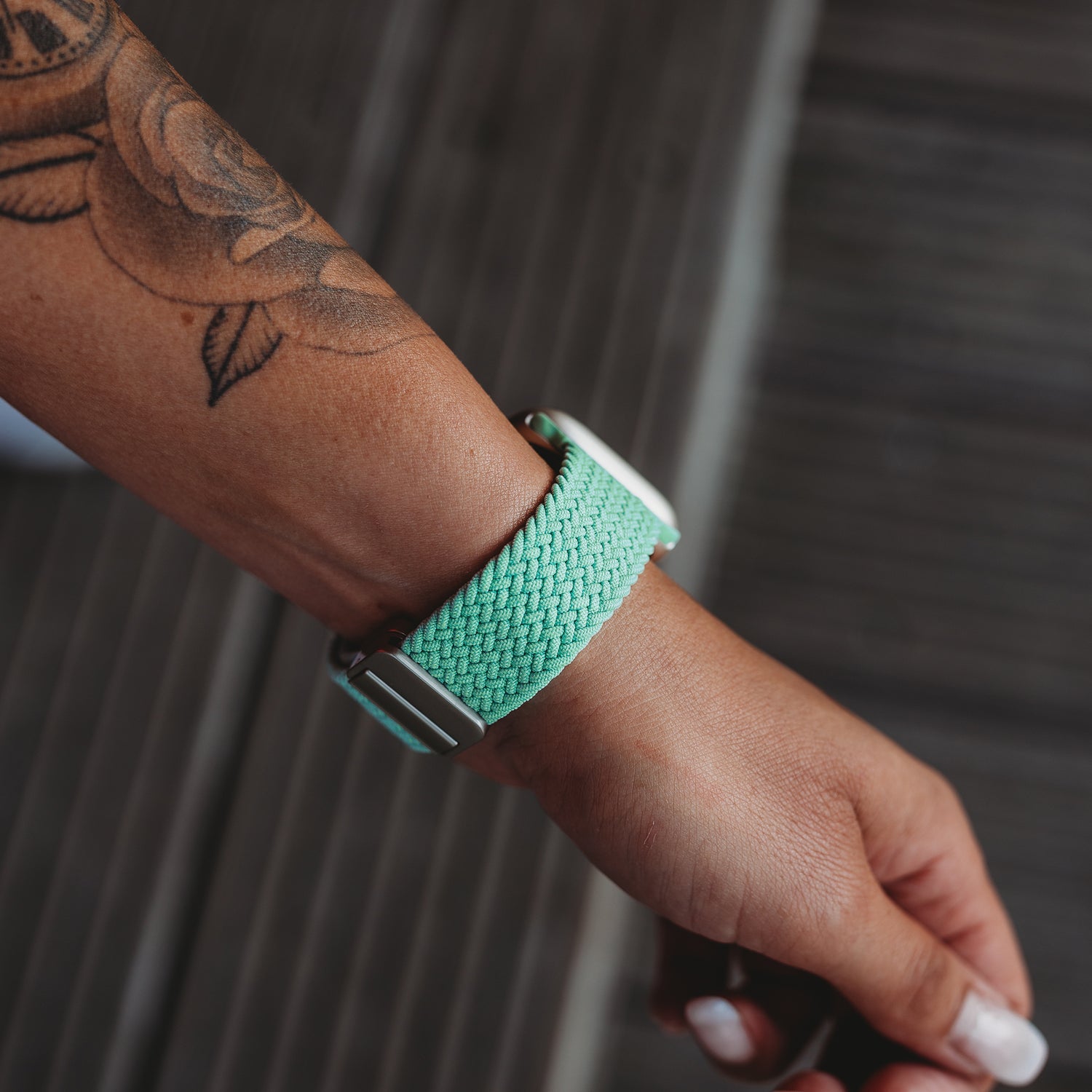 Eine Person mit einem Rosentattoo trägt ein arktisband Geflochtenes Apple Watch Armband „Casual“ mit Magnetverschluss in Mintgrün.