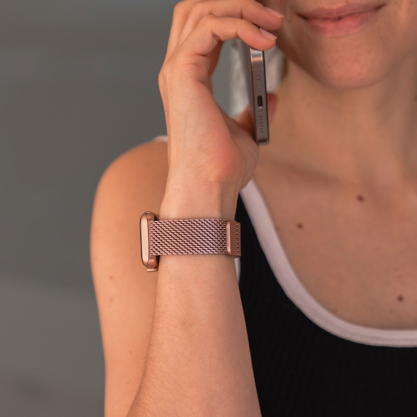 Eine Frau hält ein Telefon an ihr Ohr und trägt ein Arktisband Apple Watch Milanaise Armband „Bold“ in Pink am Handgelenk – Apple Watch kompatibel.