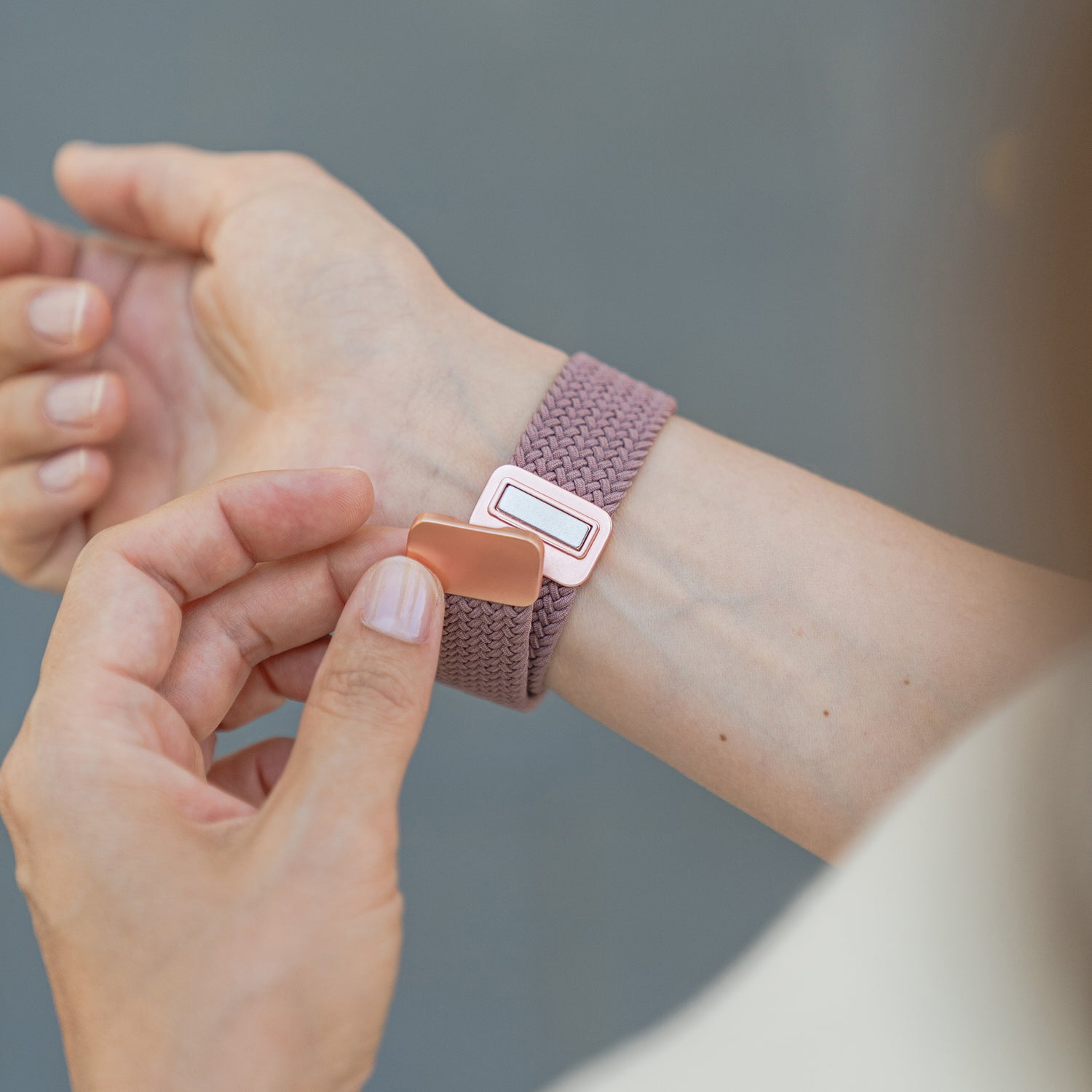 Person legt dem Künstlerband ein geflochtenes Apple Watch Armband „Casual“ mit Magnetverschluss in Pink und roségoldener Schließe am Handgelenk an – ideal für einen stilvollen Look mit der Apple Watch.