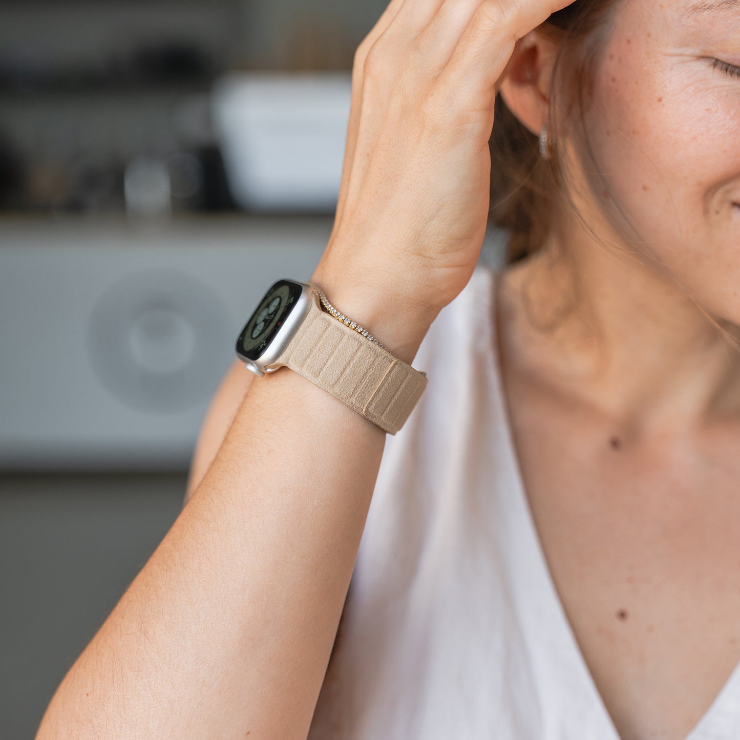 Eine Frau trägt ein Apple Watch magnetisches Armband aus Alcantara mit einem beigen Armband, hält ihre Hand an ihr Gesicht und lächelt teilweise.
