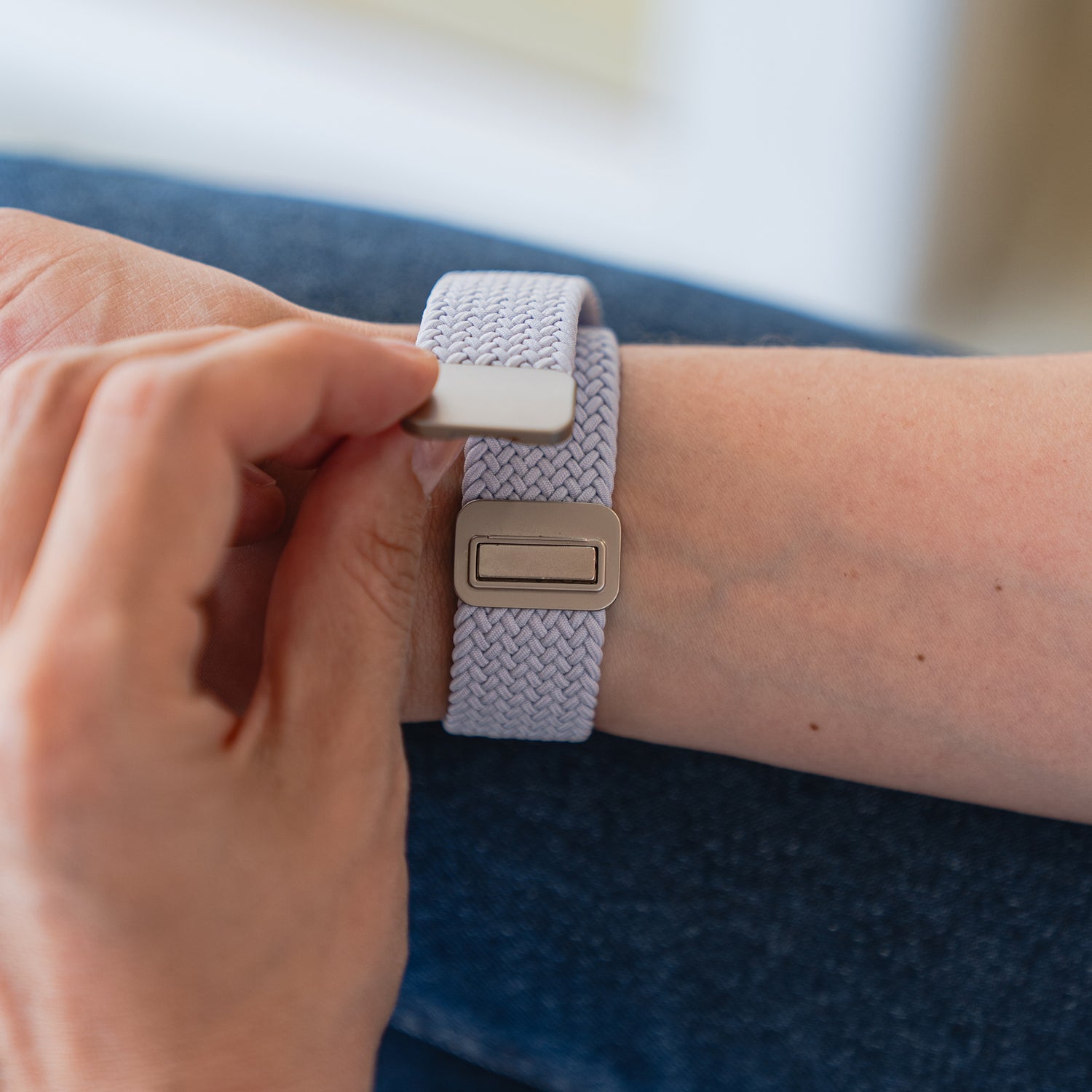 Eine Person befestigt ein kunstvoll geflochtenes Apple Watch Armband „Casual“ mit Magnetverschluss in Hellgrau an ihrem Handgelenk.