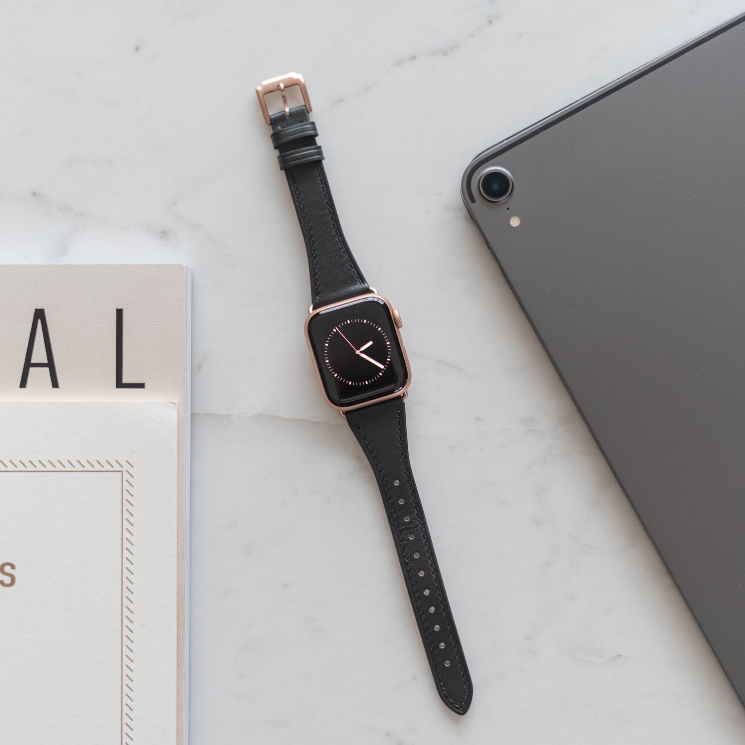 Eine schwarze Smartwatch auf einer Marmoroberfläche neben einem Tablet und einem Teil einer Zeitschrift.
