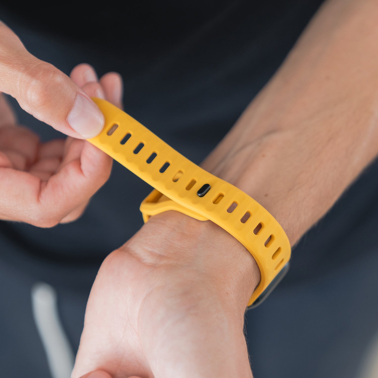 Eine Person befestigt ein Arktisband Apple Watch Silikonarmband „Active“ in Gelb um ihr Handgelenk, mit Nahaufnahme der Hände und des Handgelenks.