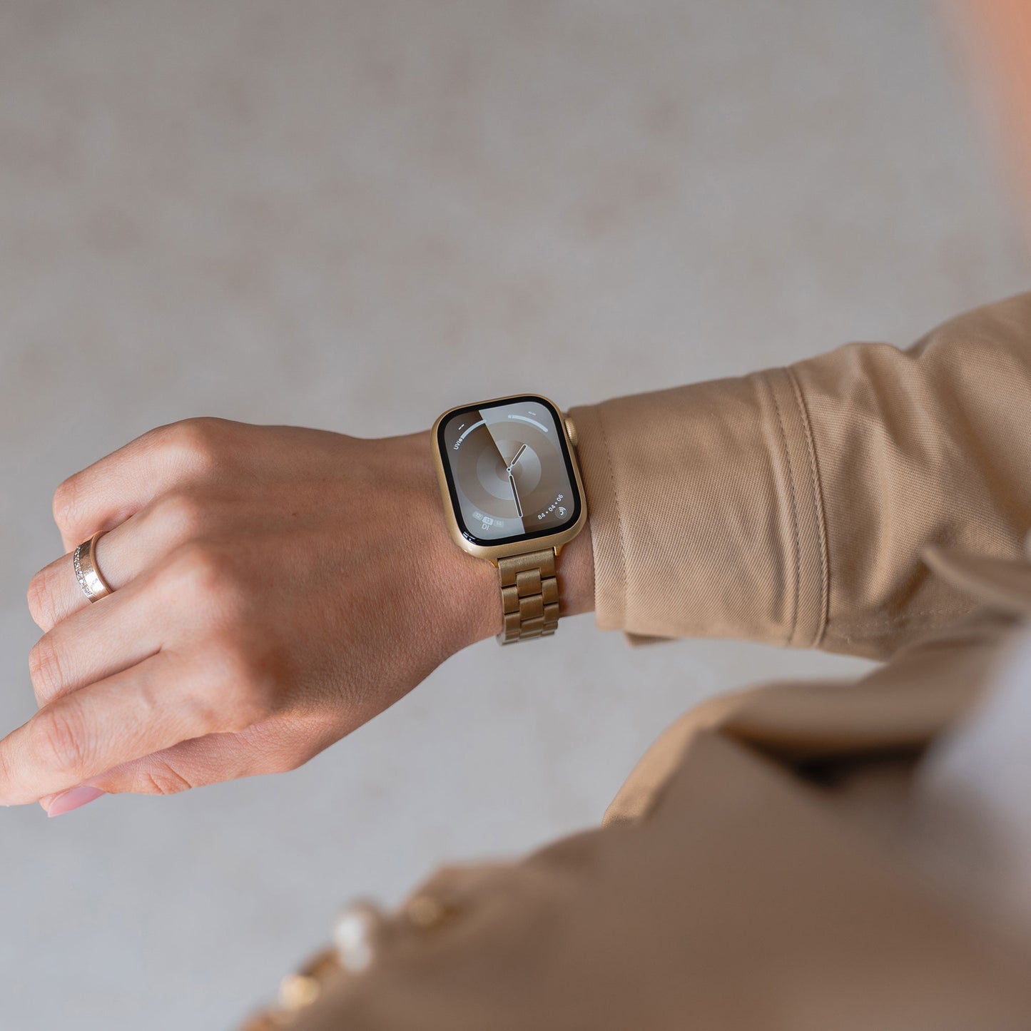 Eine Person trägt ein goldenes Arktisband Apple Watch Gliederarmband „Arctica“ – Slim mit modernem Ziffernblatt und beigem Mantel.