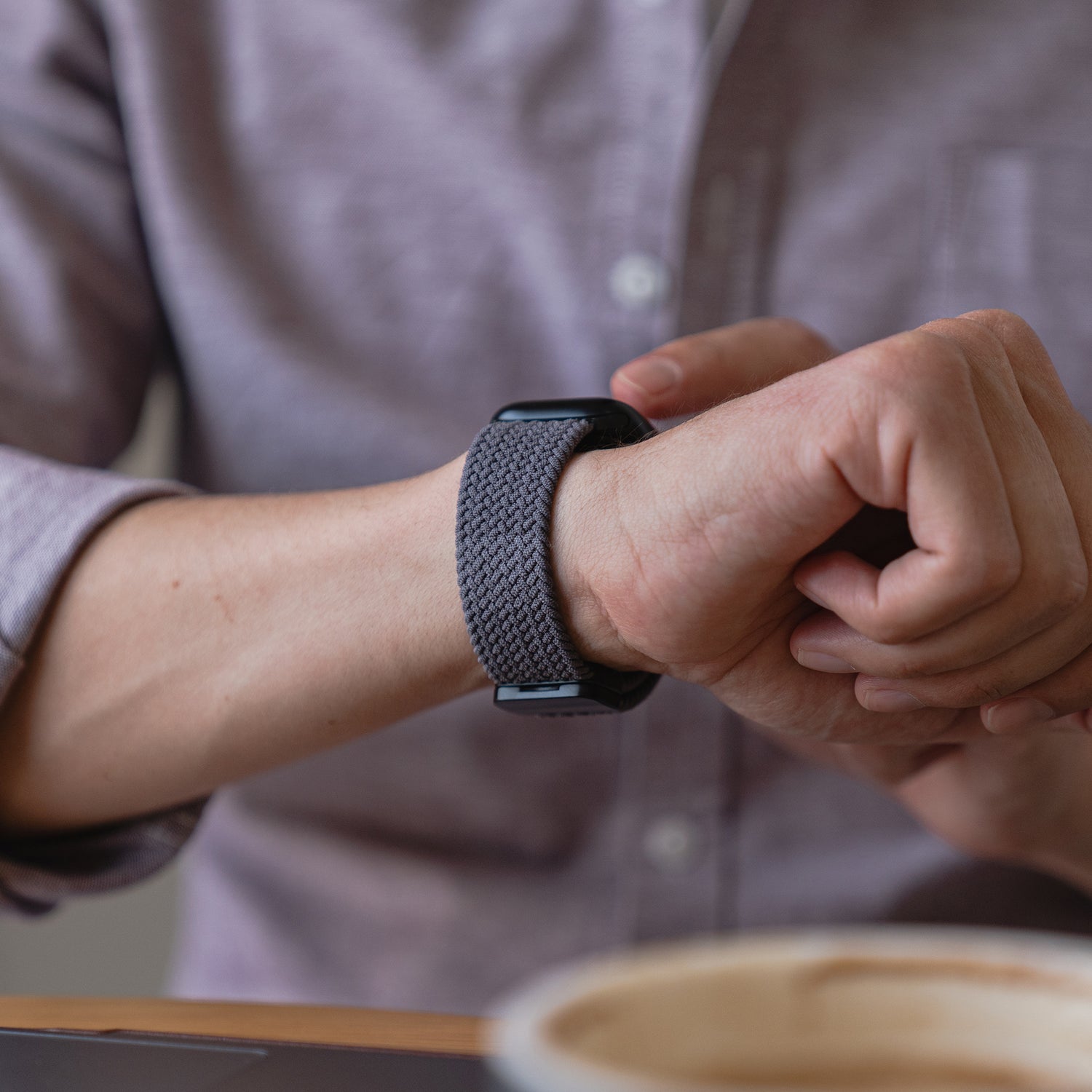 Jemand in einem lila Hemd prüft sein geflochtenes Apple Watch Armband „Casual“ mit Magnetverschluss am linken Handgelenk.