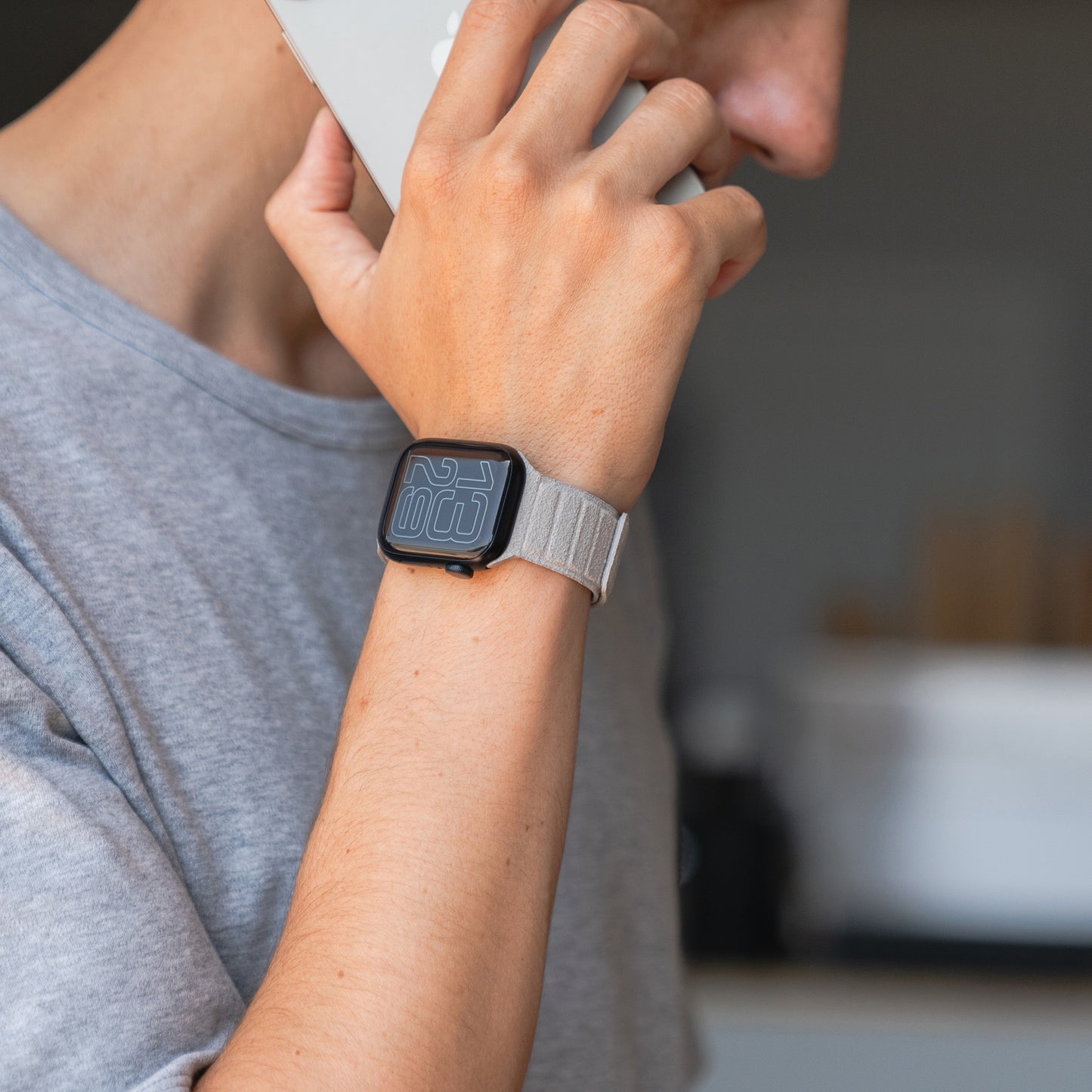 Eine Person, die eine Apple Watch von arktisband magnetisches Armband aus Alcantara by arktisband auf ihrer Smartwatch trägt, bekleidet mit einem grauen Hemd, hält sich ein Smartphone ans Ohr.