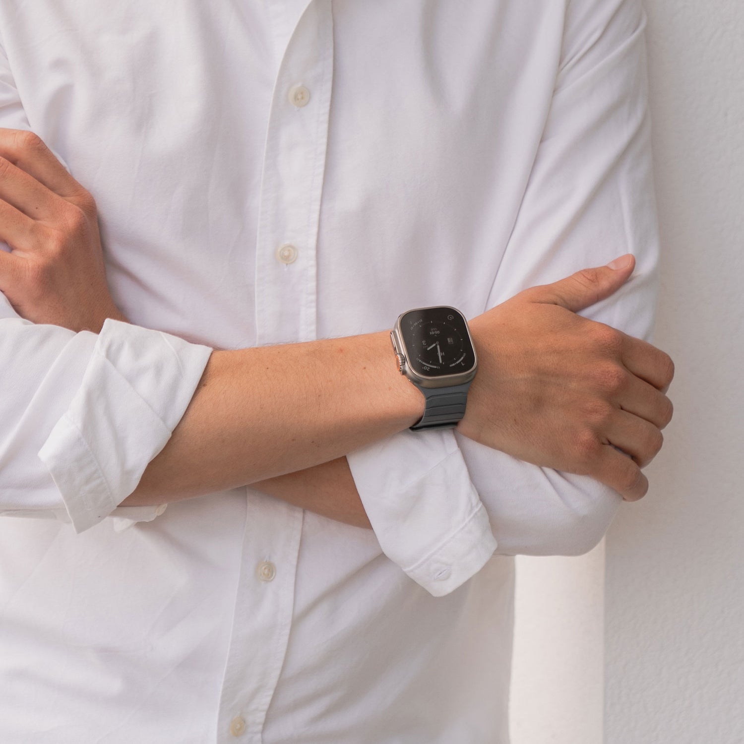 Eine Person in einem weißen Hemd mit Knöpfen verschränkt die Arme und präsentiert das magnetische Apple Watch Armband „MagFlow“ an ihrem linken Handgelenk. Das Bild ist von den Schultern abwärts zugeschnitten.