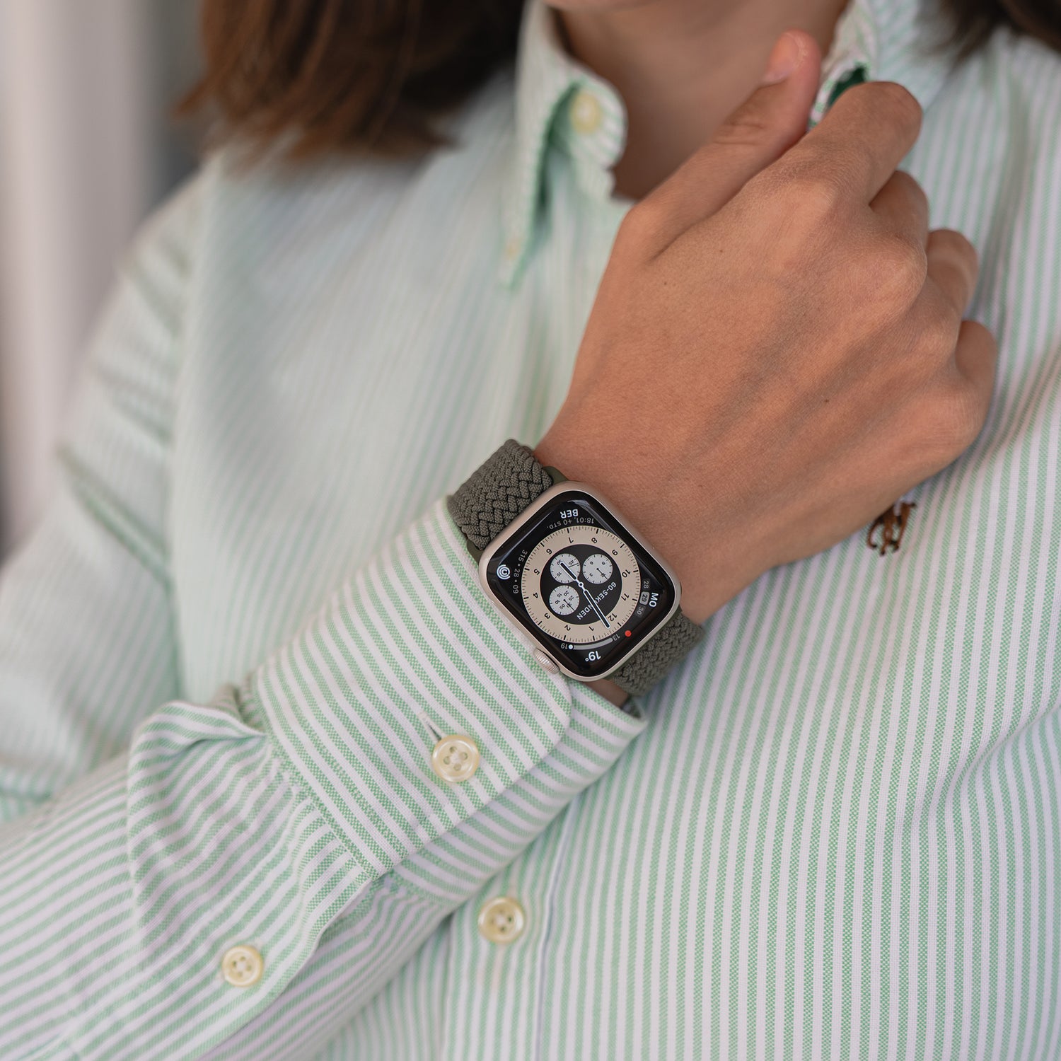 Eine Person in einem grün-weiß gestreiften Hemd überprüft ihr arktisband Geflochtenes Apple Watch Armband „Casual“ mit Magnetverschluss.