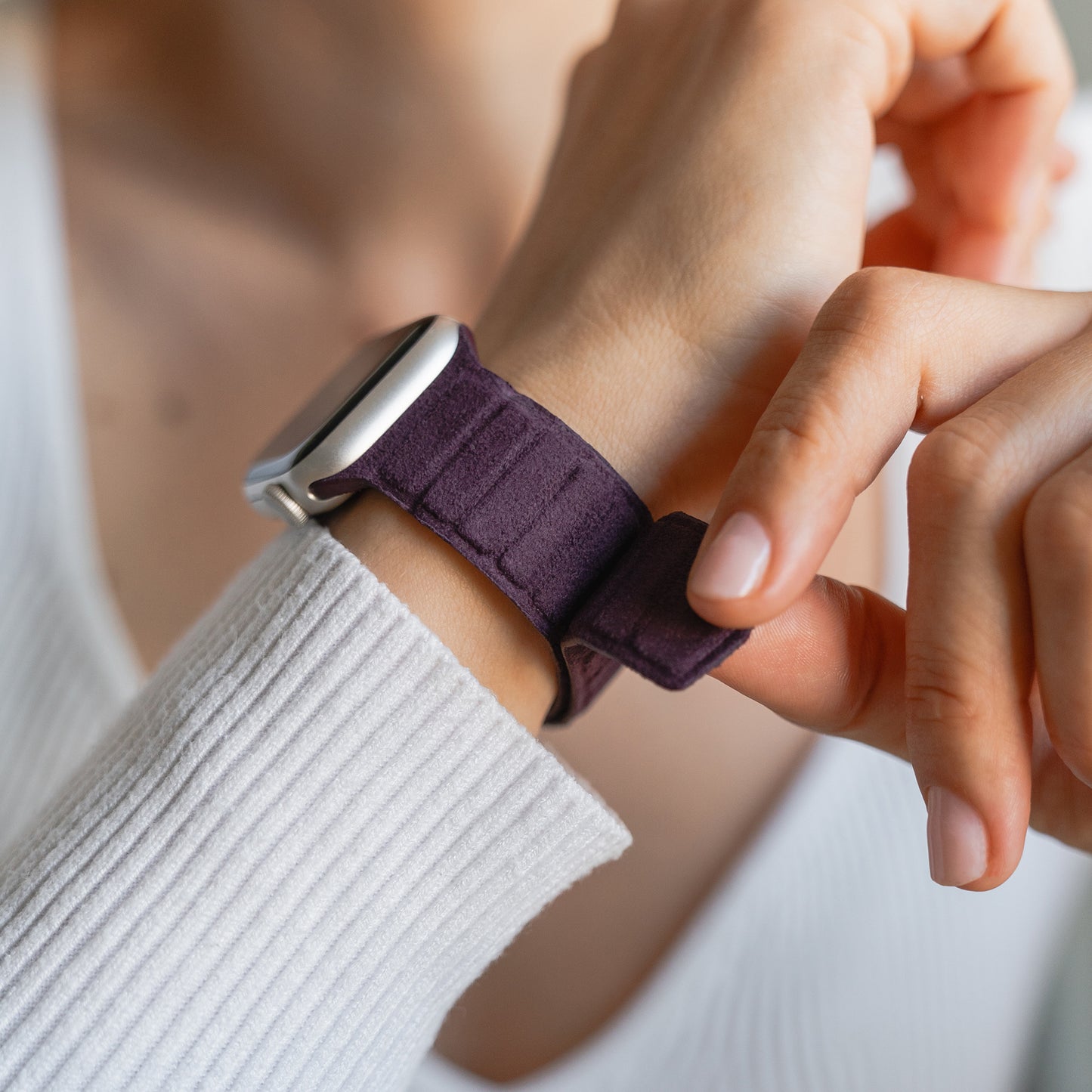 Nahaufnahme einer Person, die ein Apple Watch magnetisches Armband aus Alcantara in dunklem Lila an ihrem Handgelenk anbringt, das echtes italienisches Lebensgefühl vermittelt.