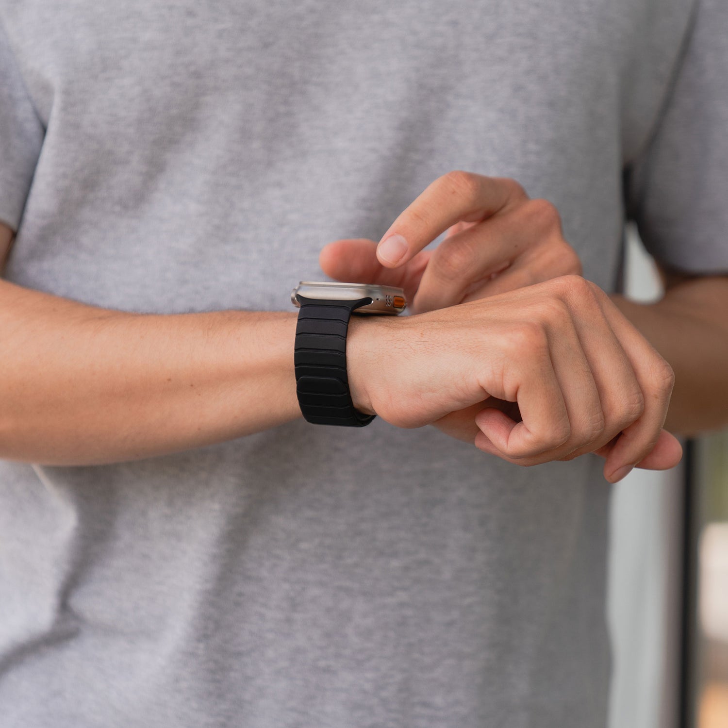 Person trägt ein graues T-Shirt und benutzt das arktisband Apple Watch magnetisches Armband „MagFlow“ aus Silikon mit magnetischem Halt am linken Handgelenk.