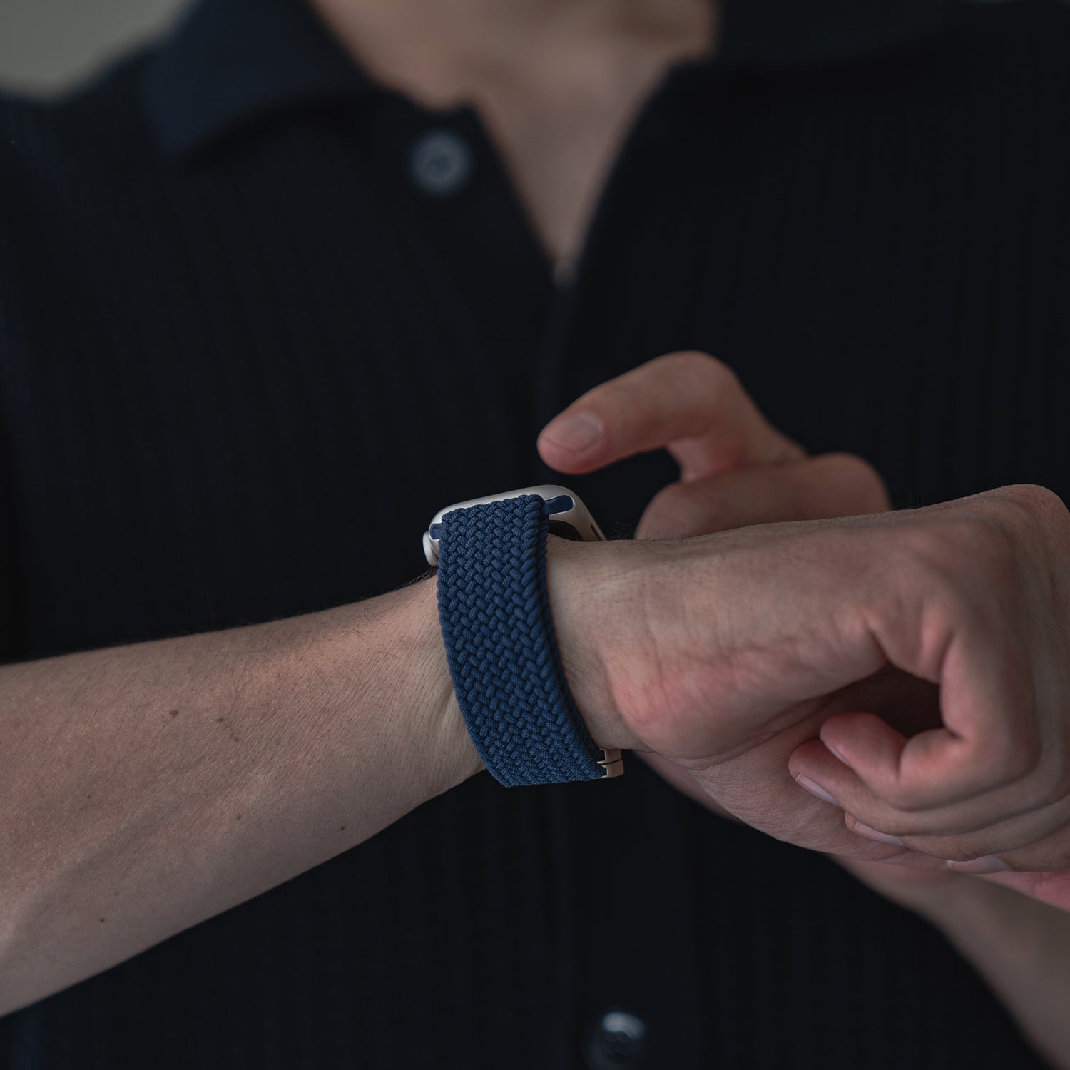 Eine Person trägt ein Arktisband Geflochtenes Apple Watch Armband „Casual“ mit Magnetverschluss in Marineblau am linken Handgelenk und tippt mit der rechten Hand auf den Bildschirm der Apple Watch.