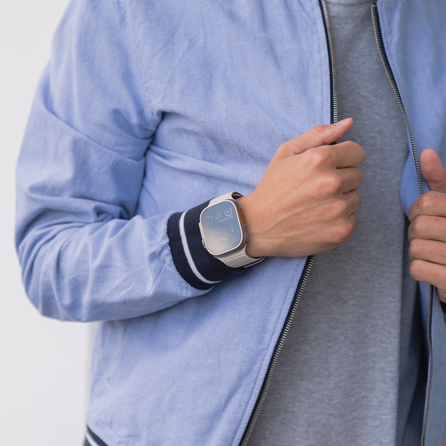 Eine Person in hellblauem Jackett trägt das Artisband Apple Watch Magnetarmband „MagFlow“ aus Silikon und passt den Reißverschluss ihrer Jacke an.