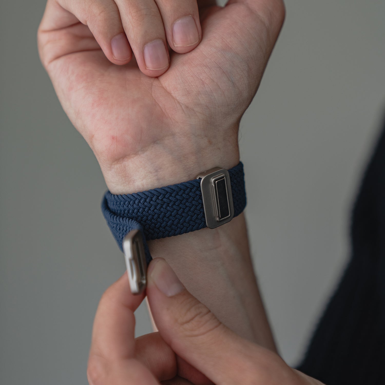 Eine Hand befestigt das blaue arktisband Geflochtene Apple Watch Armband „Casual“ mit Magnetverschluss von arktisband an ihrem Handgelenk.