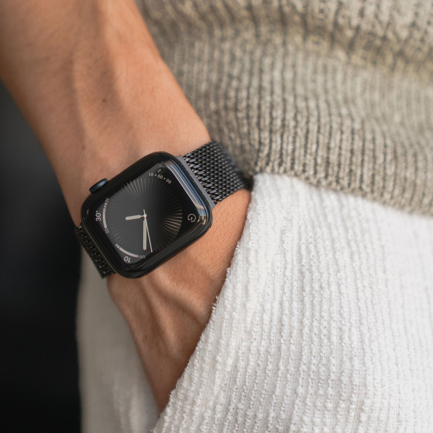 Jemand trägt ein arktisband Apple Watch Milanaise Armband "Bold" mit der Hand in der Tasche einer strukturierten weißen Hose.