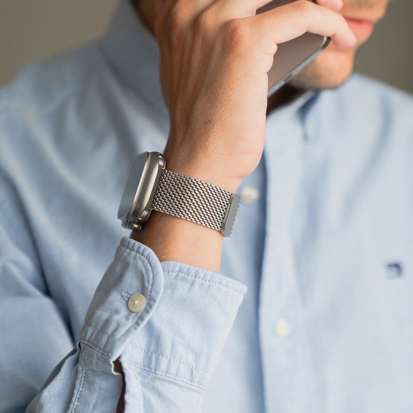 Mann im blauen Hemd hält sich ein Telefon ans Ohr und trägt ein elegantes Arktisband Apple Watch Milanaise Armband "Bold" mit Magnetverschluss am Handgelenk.