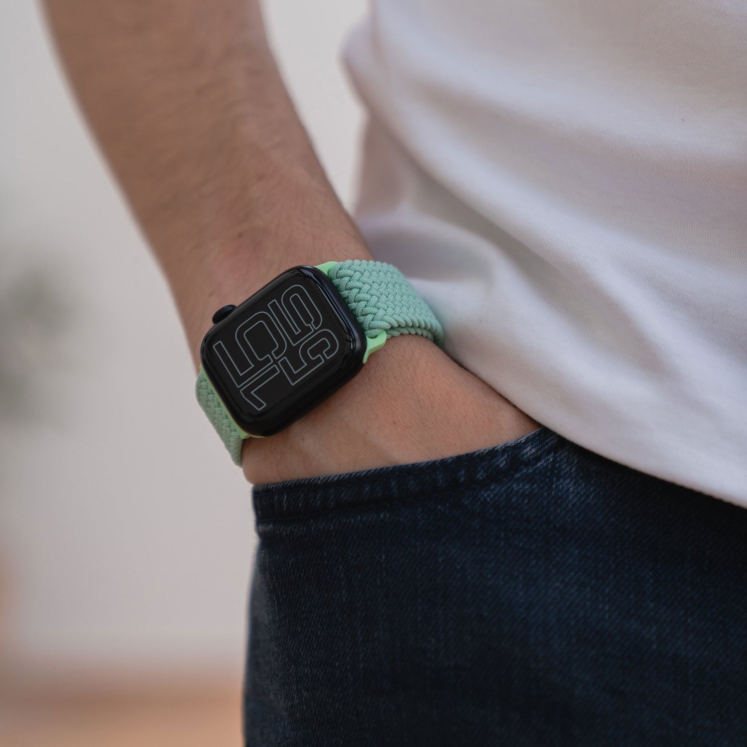 Person trägt ein arktisband Geflochtenes Apple Watch Armband „Casual“ mit Magnetverschluss in grün, Hand in der Tasche, dazu Jeans und weißes Shirt.