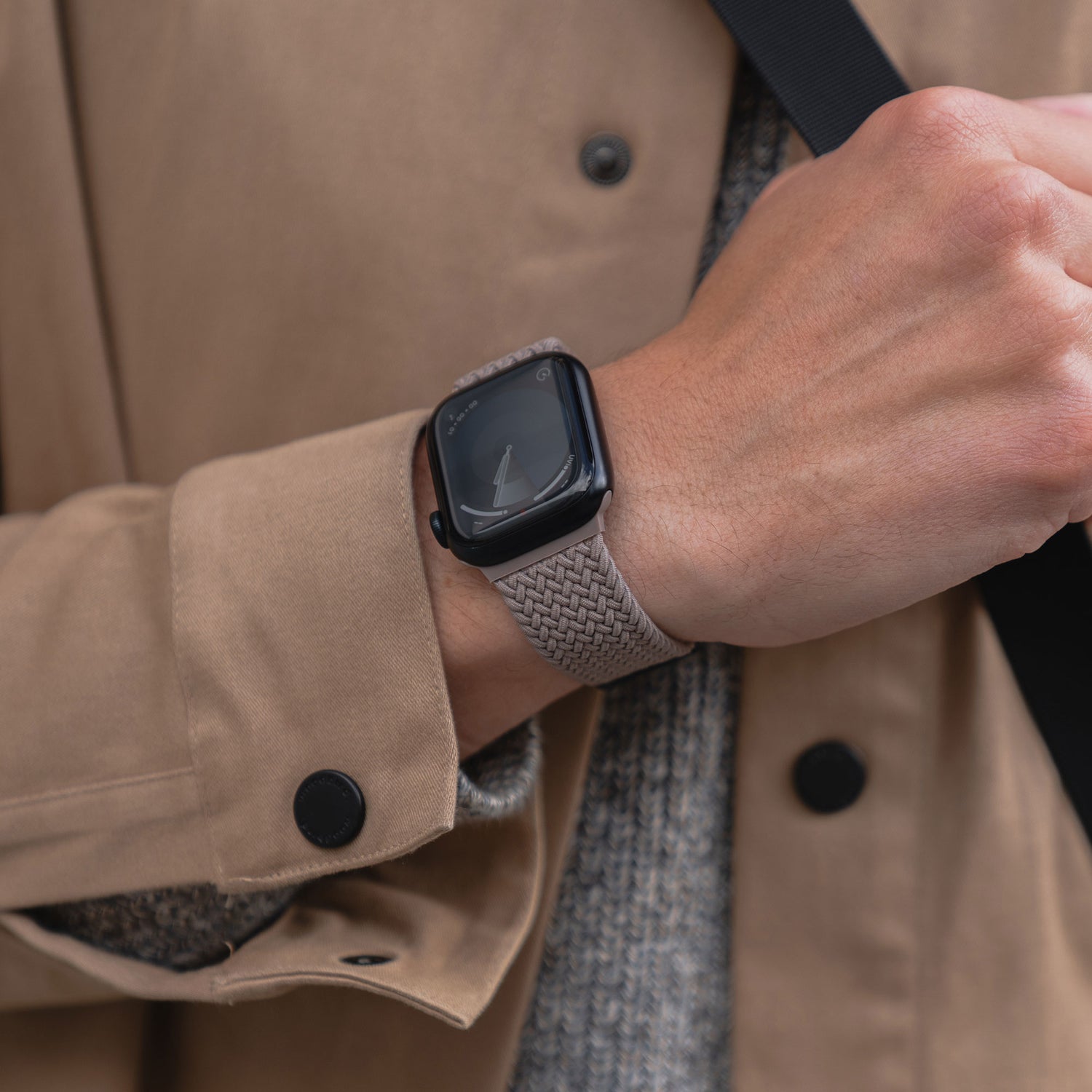 Eine Person trägt ein arktisbandgeflochtenes Apple Watch Armband „Casual“ mit Magnetverschluss und einen braunen, geknöpften Mantel.