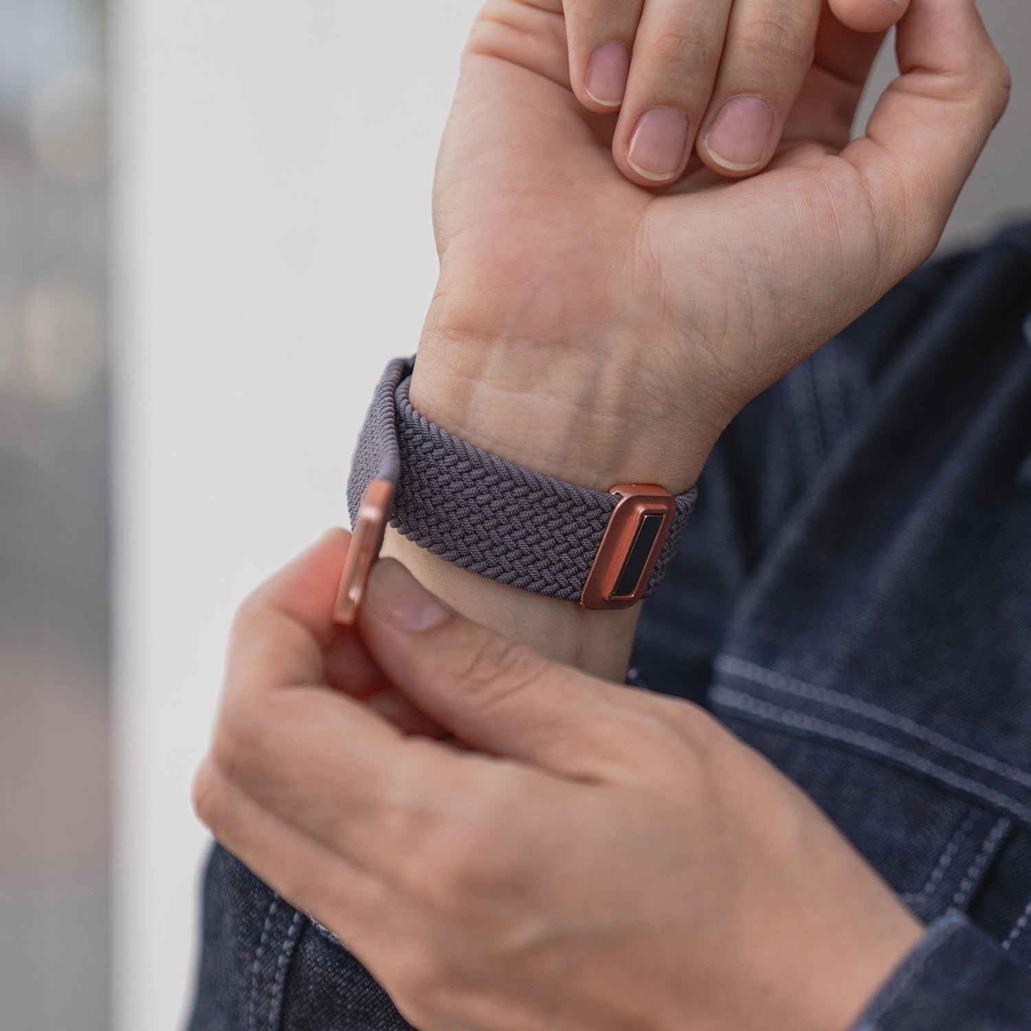 Eine Person legt das kunstvoll geflochtene Apple Watch Armband „Casual“ mit Magnetverschluss in Lila und roségoldener Schließe ums Handgelenk.
