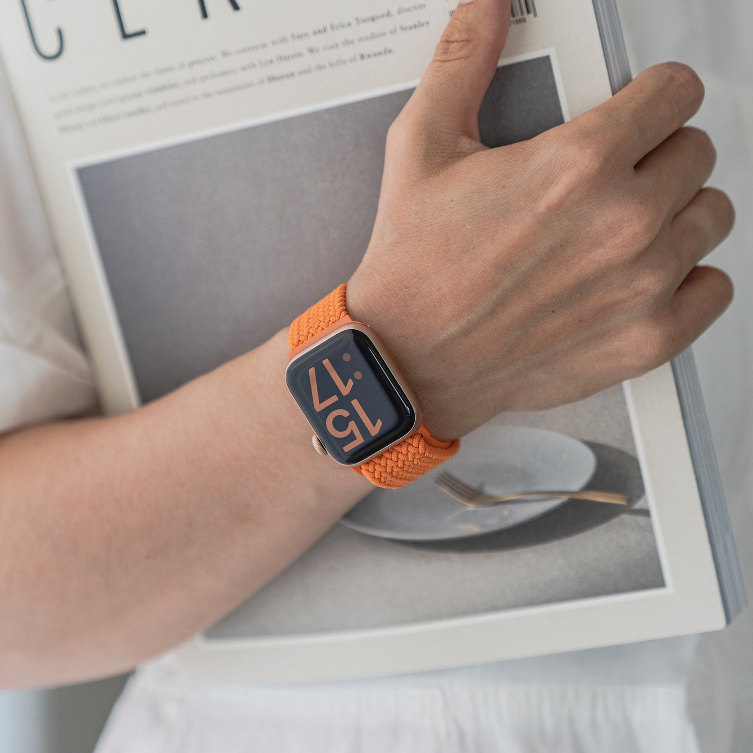 Eine Person, die ein Arktisband-geflochtenes Apple Watch Armband „Casual“ mit Magnetverschluss trägt, hält eine Zeitschrift mit einem Teller und einer Gabel auf dem Cover.
