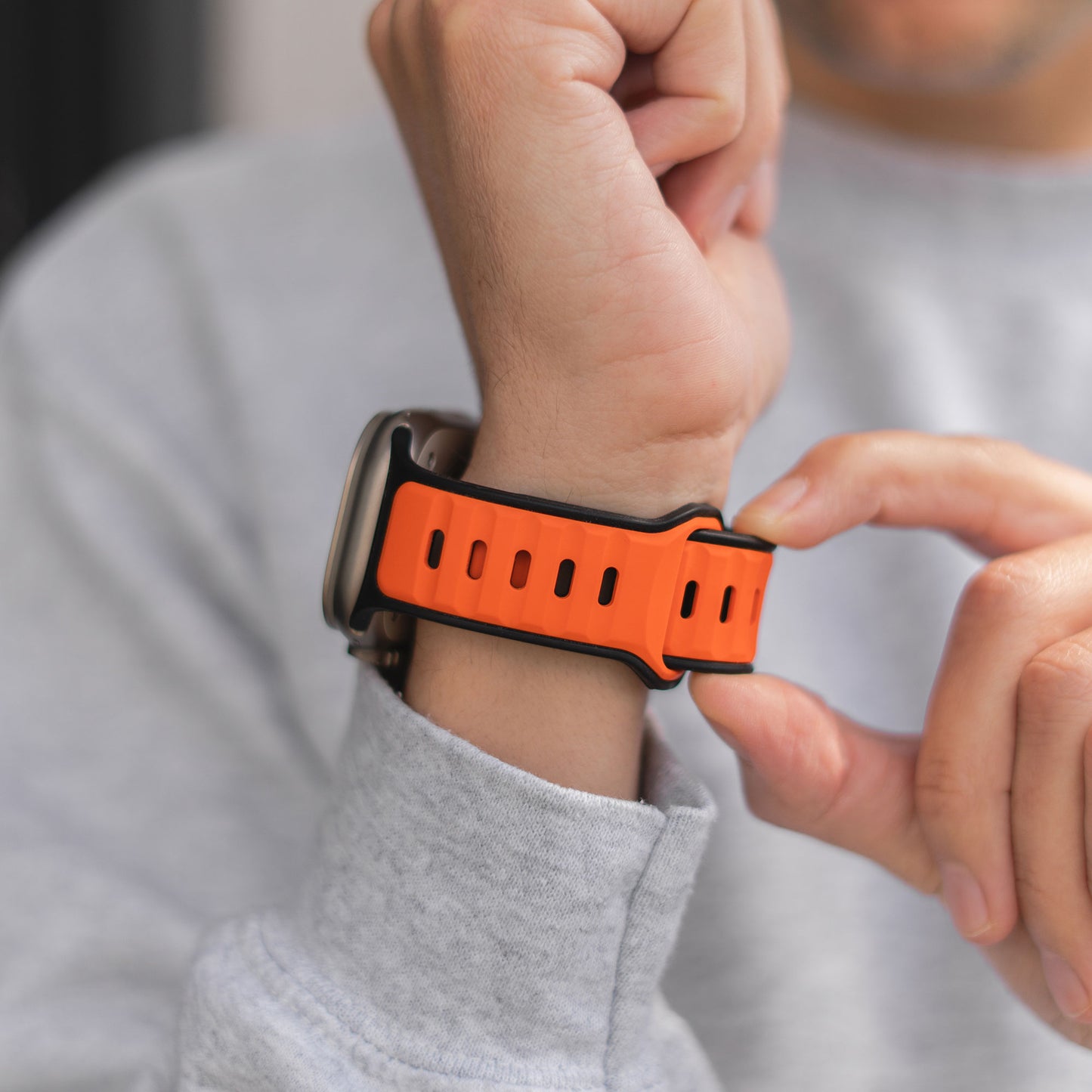 Nahaufnahme einer Person, die das Arktisband Apple Watch Silikonarmband „Swift“ in Orange trägt und den Aluminium-Pin-Verschluss des Armbands einstellt.